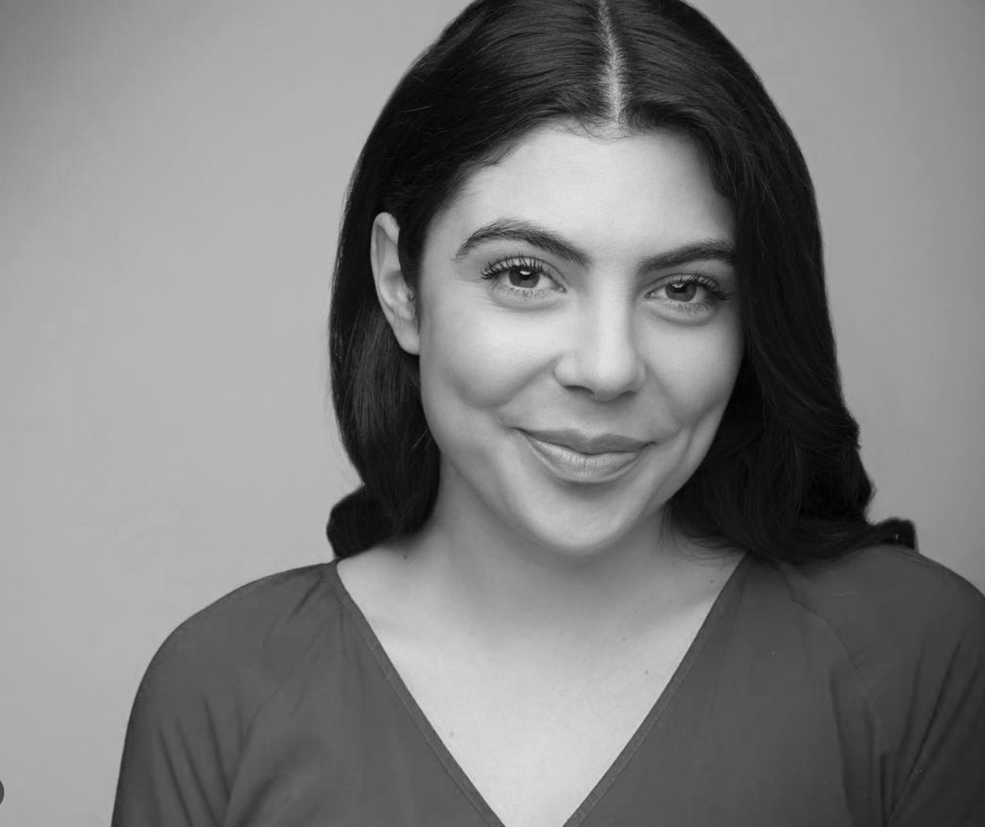Black and white portrait of a woman with shoulder-length dark hair, smiling softly, wearing a V-neck top, against a plain background.