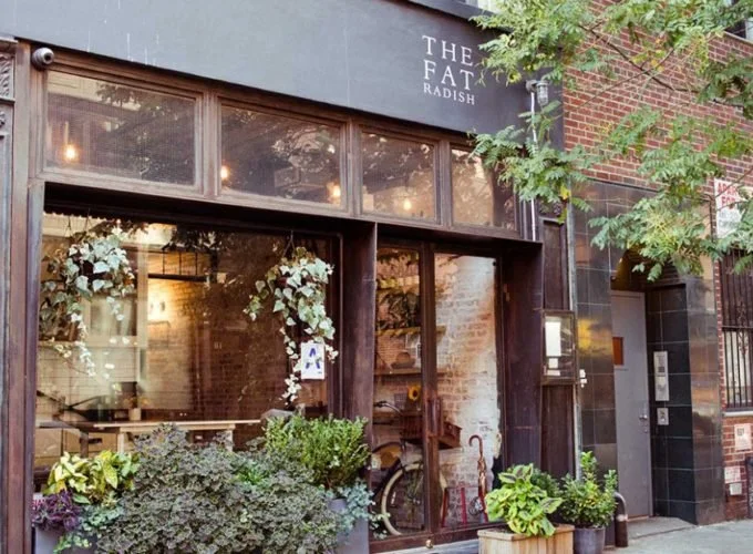 Facade of The Fat Radish restaurant with large glass windows and greenery outside.