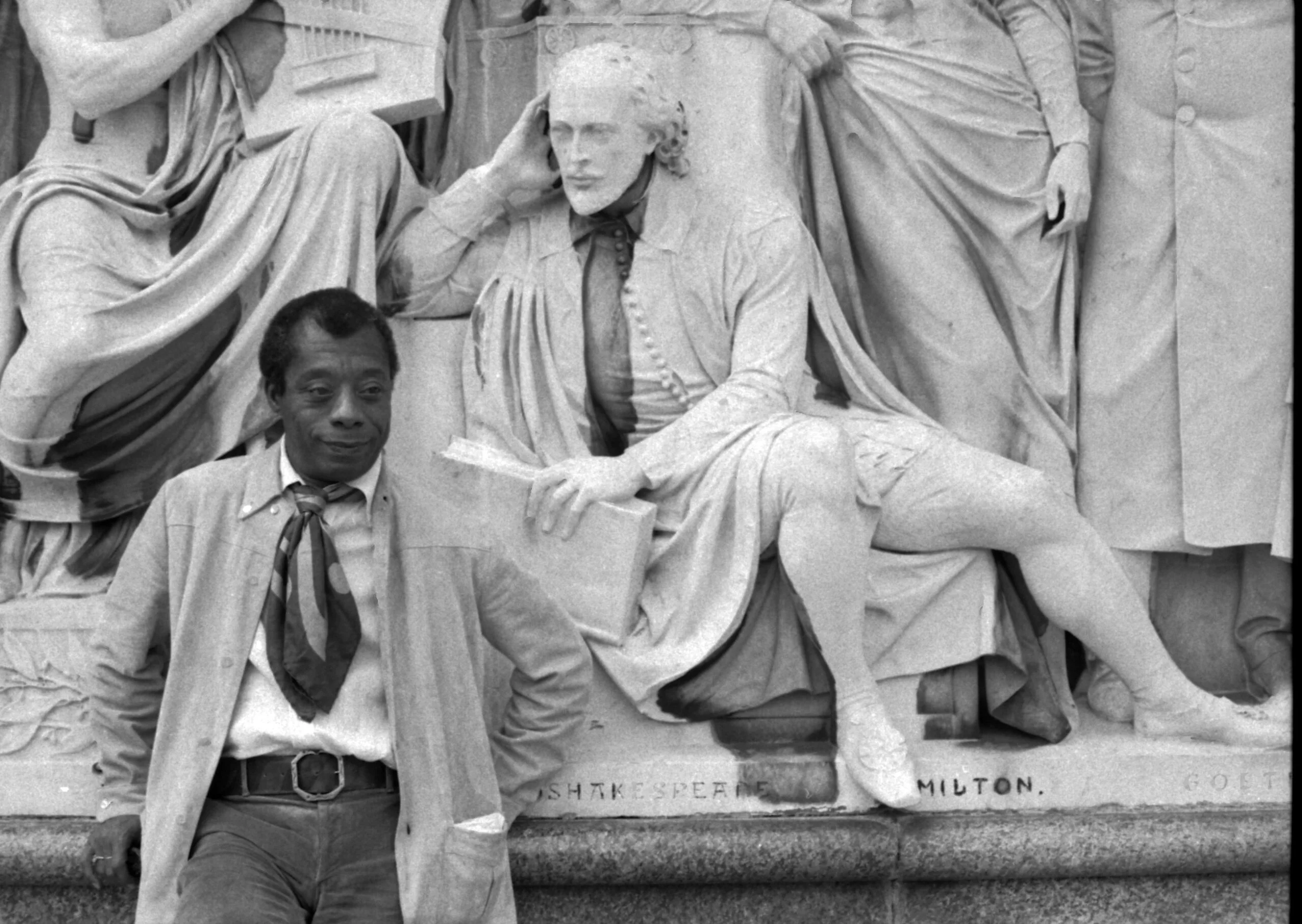 A man standing in front of the Lincoln Memorial statue in Washington, D.C., with one hand on his hip and the other arm relaxed, wearing a light-colored jacket and a patterned scarf.