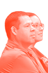 Side view of two people seated, with the person in the foreground having short hair and wearing a striped shirt, and the person in the background with glasses. The image has an orange-red filter overlay.