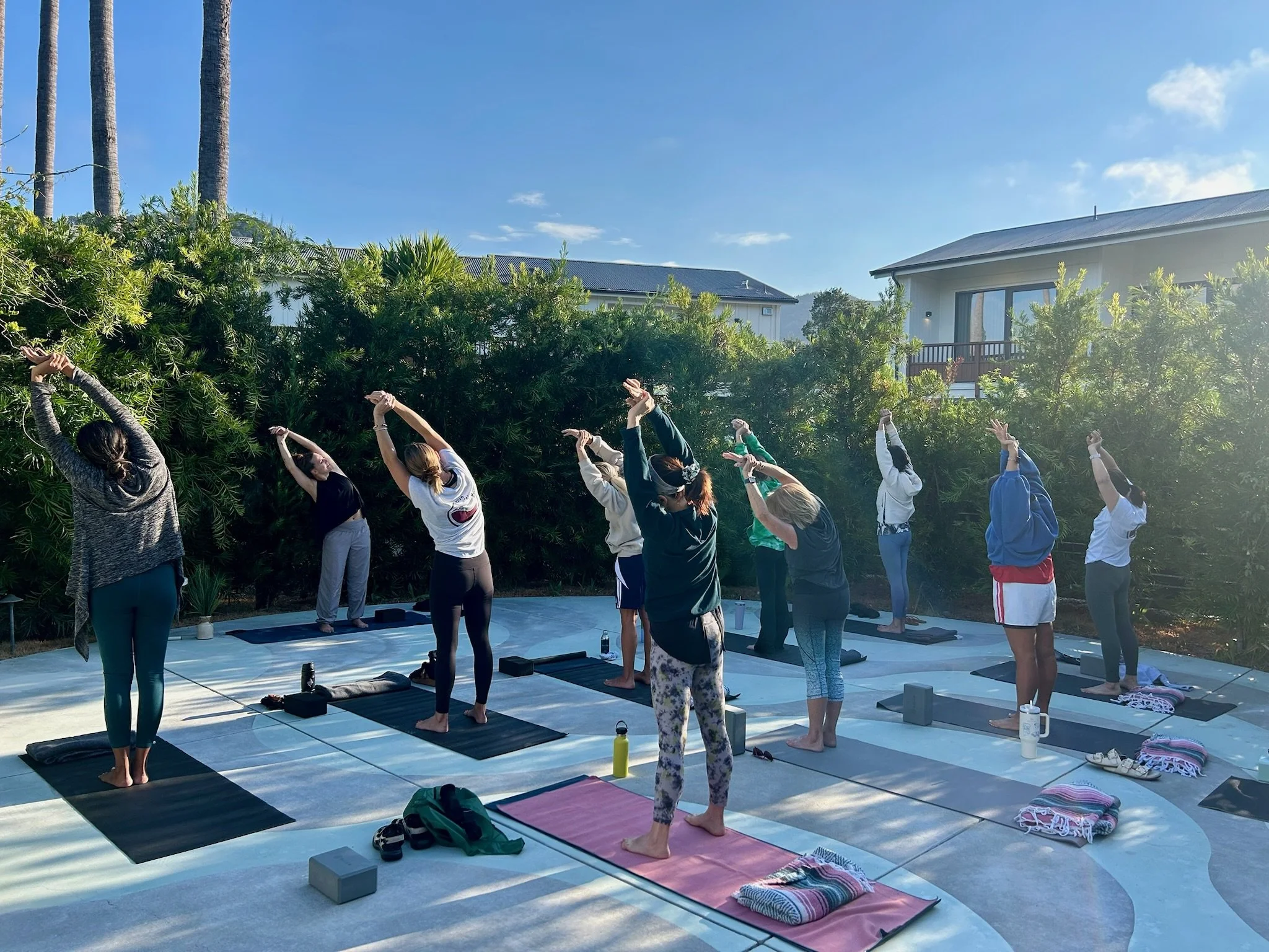 Group of people participating in outdoor yoga class on a sunny day, standing on mats with arms stretched overhead at resort in Calistoga, CA.