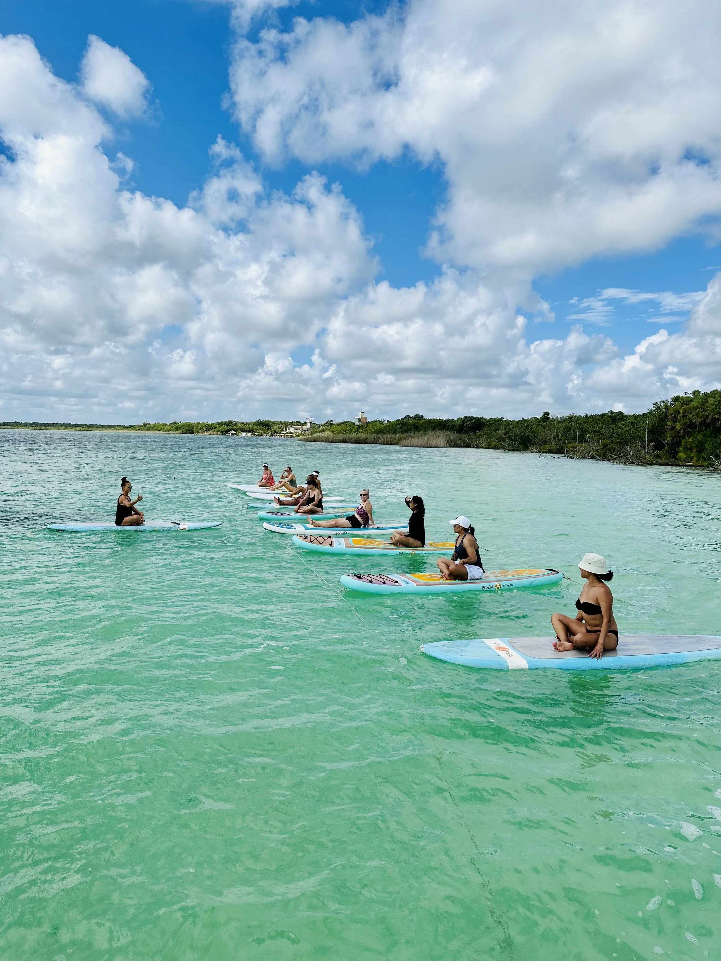 Group of people practicing yoga on stand-up paddleboards in clear, calm water under a partly cloudy sky.
