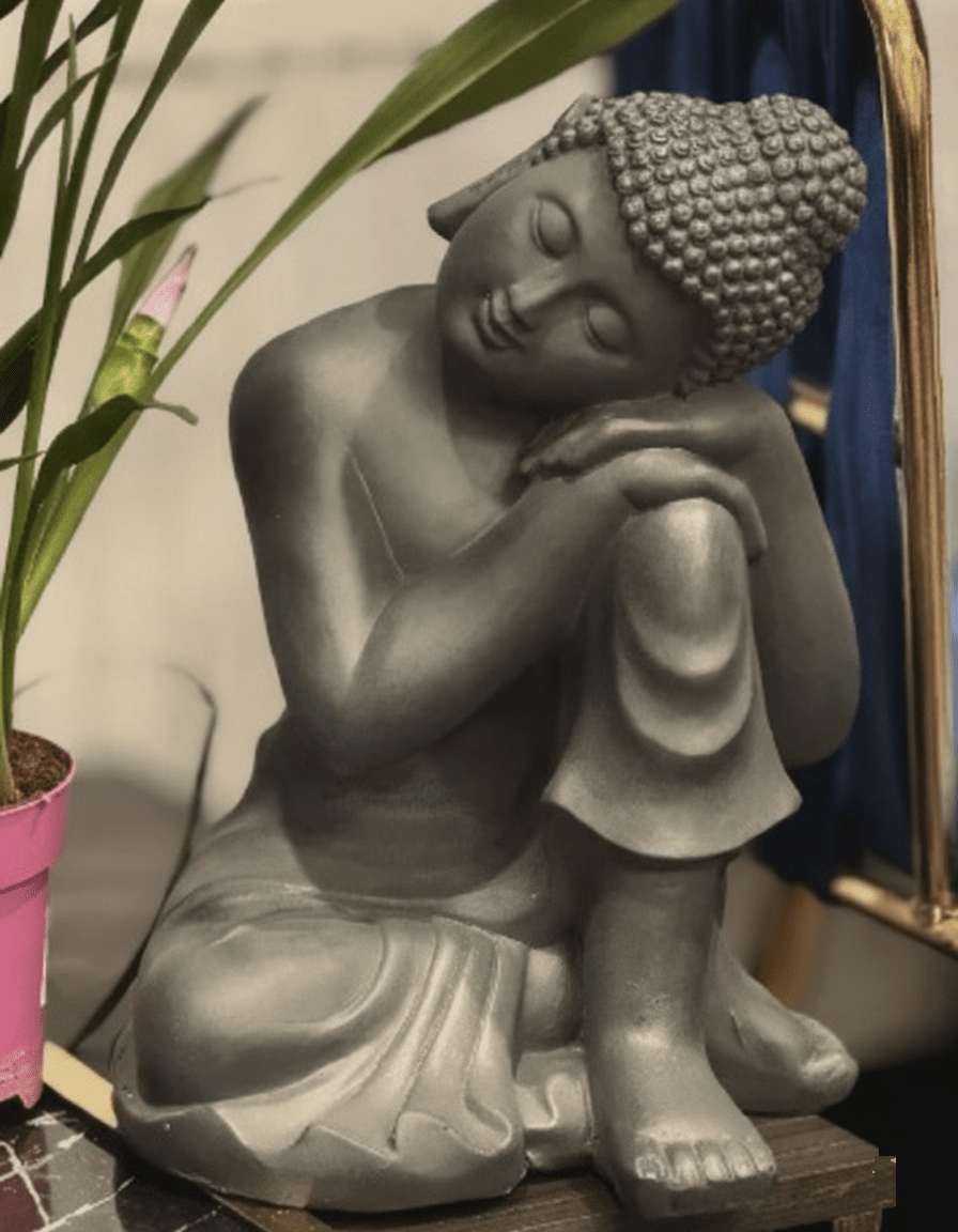 Ramybės oazė „Alispa“ salone. Pilka medituojančio Budos statula ir augalai, kuriantys atpalaiduojančią atmosferą.