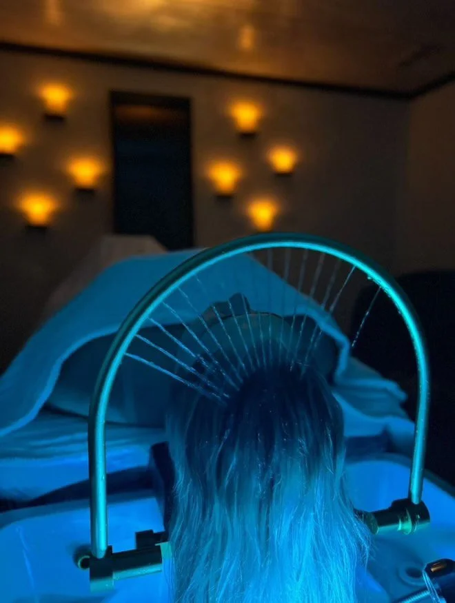 Galvos odos gydomoji procedūra su mėlyna šviesa. SPA terapija tamsiame, jaukiame kambaryje.