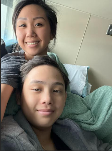 A woman and a young man lying on a hospital bed, smiling at the camera.