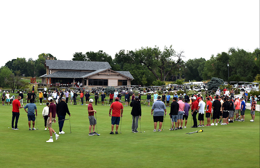 People lined up on a golf course during daytime for a gathering or event.