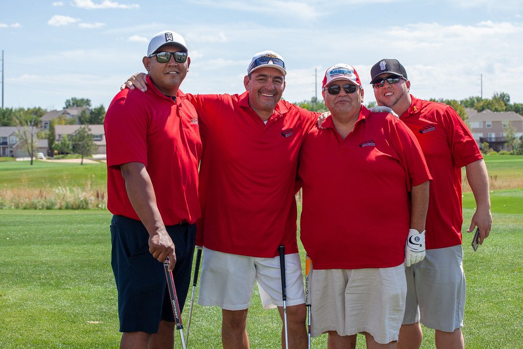 Group of five men in red shirts standing together on a golf course.
