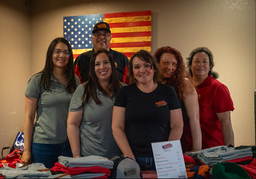 Five people standing behind a table with folded clothes and a sign, with an American flag in the background.