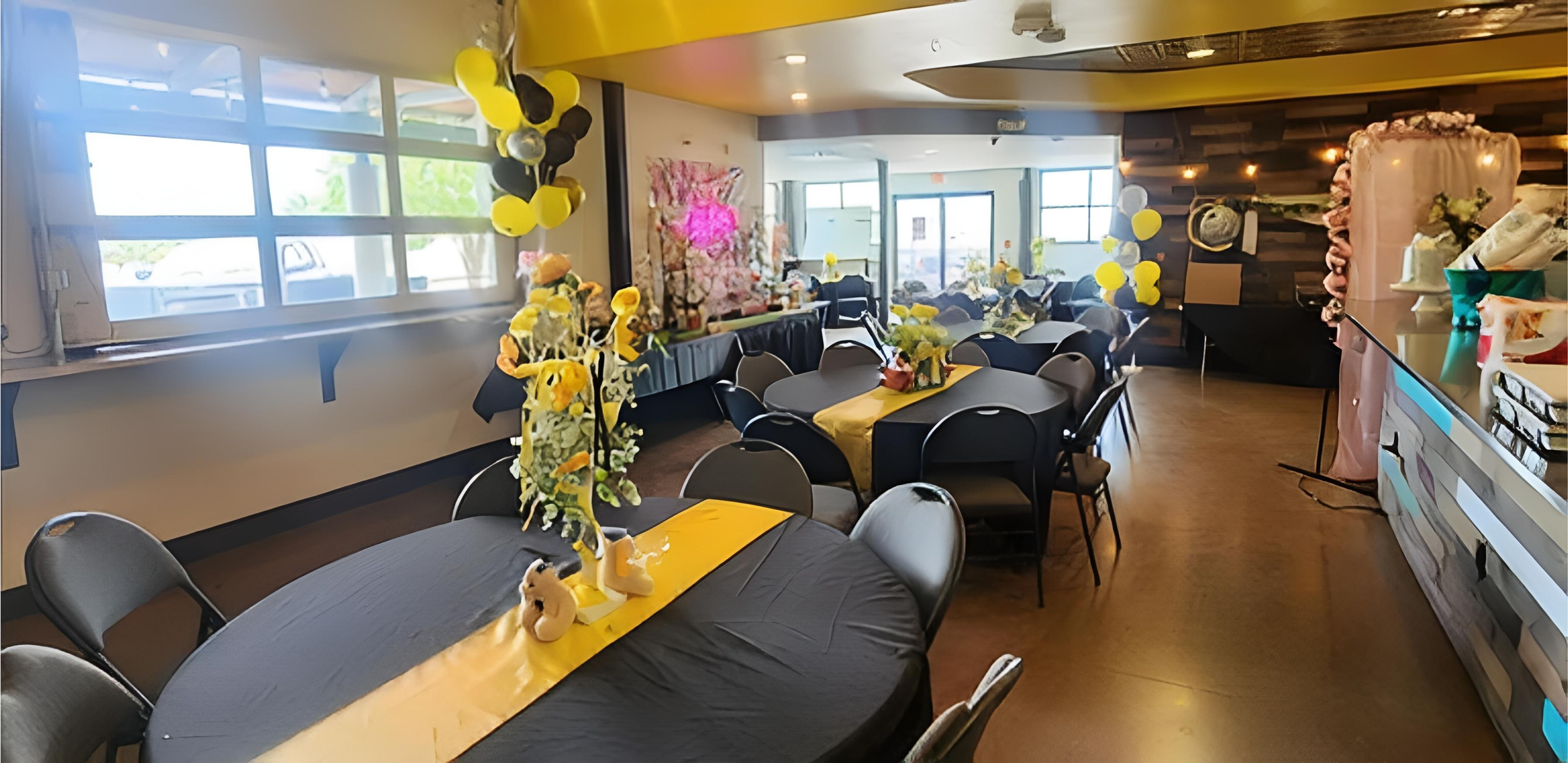 Decorated indoor party room with tables, chairs, and yellow and black balloon centerpieces for a celebration or event.