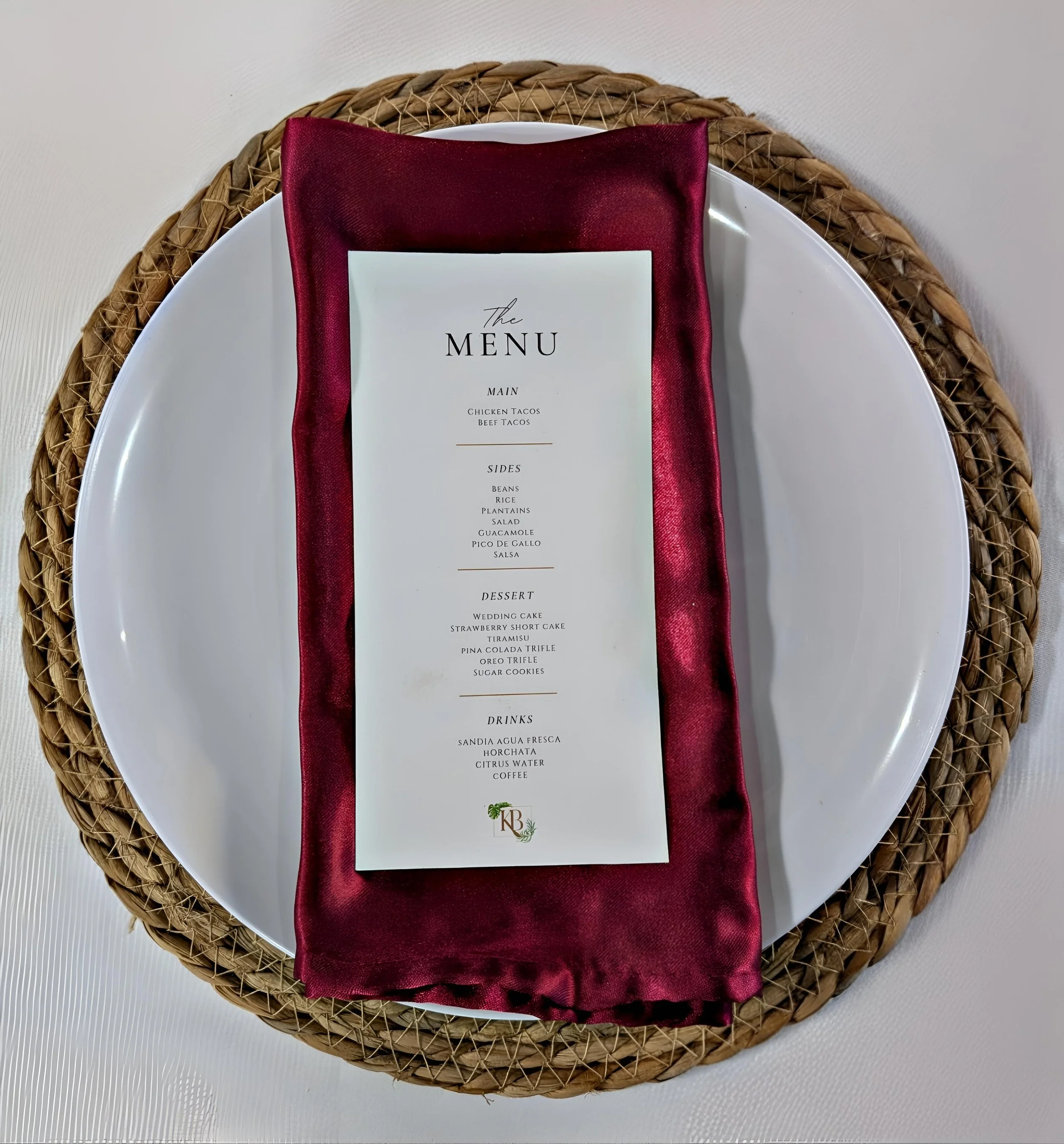 A table setting with a white plate on a woven placemat, covered by a burgundy cloth napkin, and a printed menu placed on top.