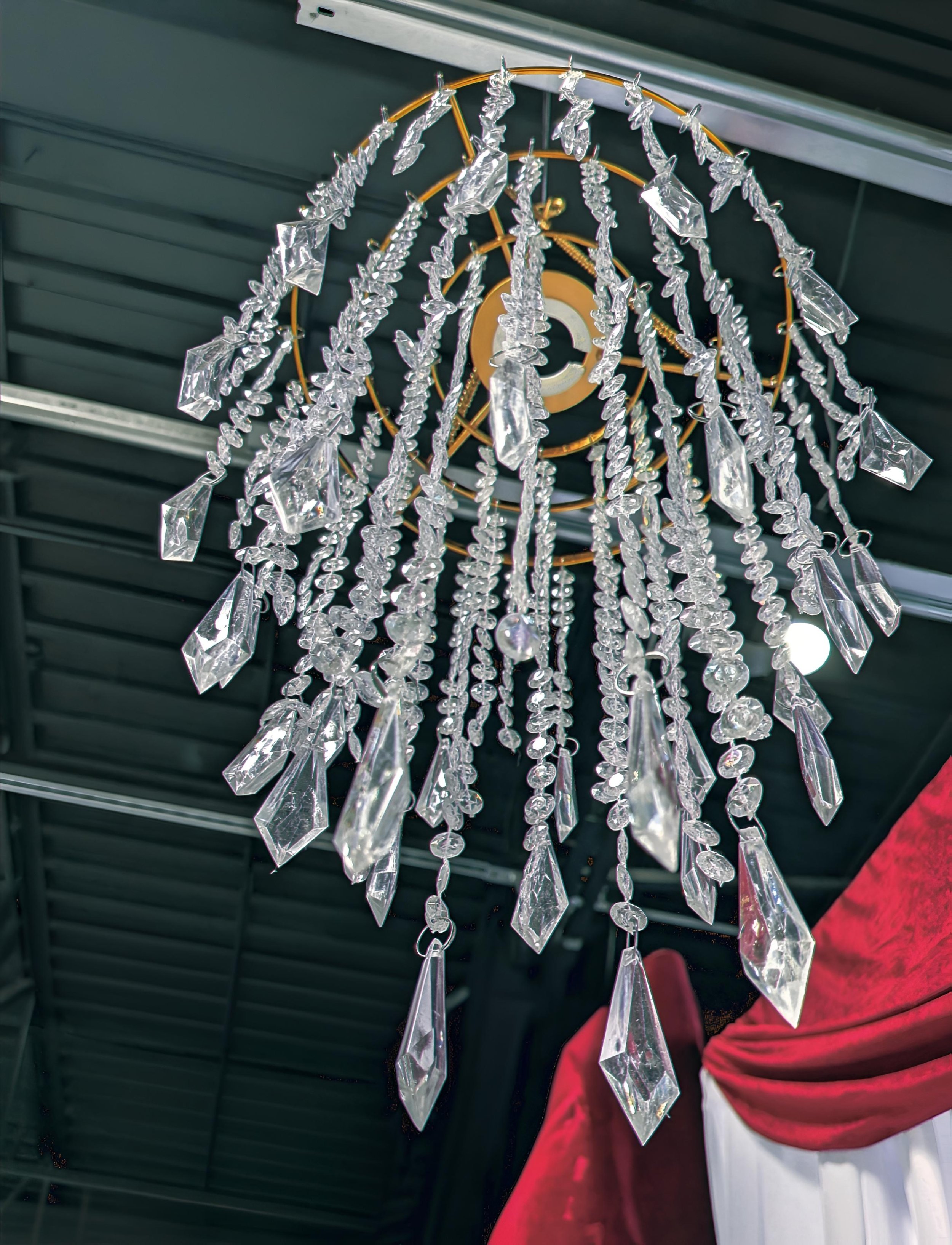 Close-up view of a crystal chandelier with multiple hanging crystal prisms and beads, mounted on a ceiling with metal framework.