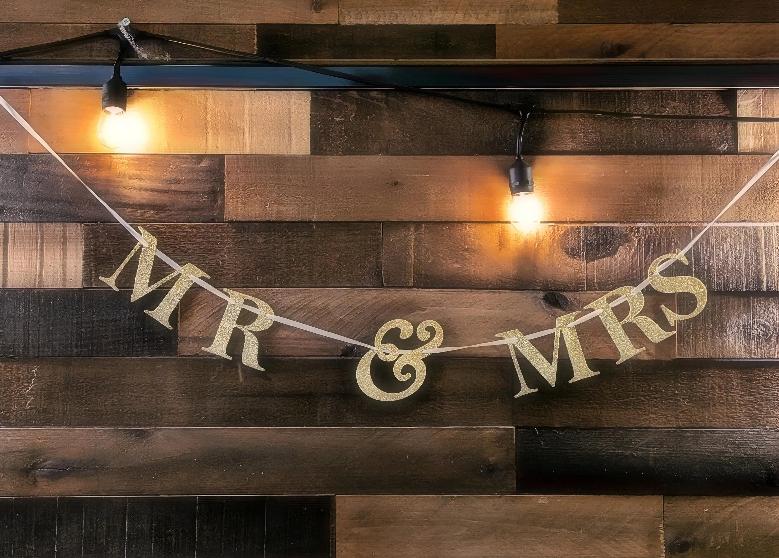 Decorative 'Merry & Misters' banner on a wooden wall with two exposed light bulbs overhead.