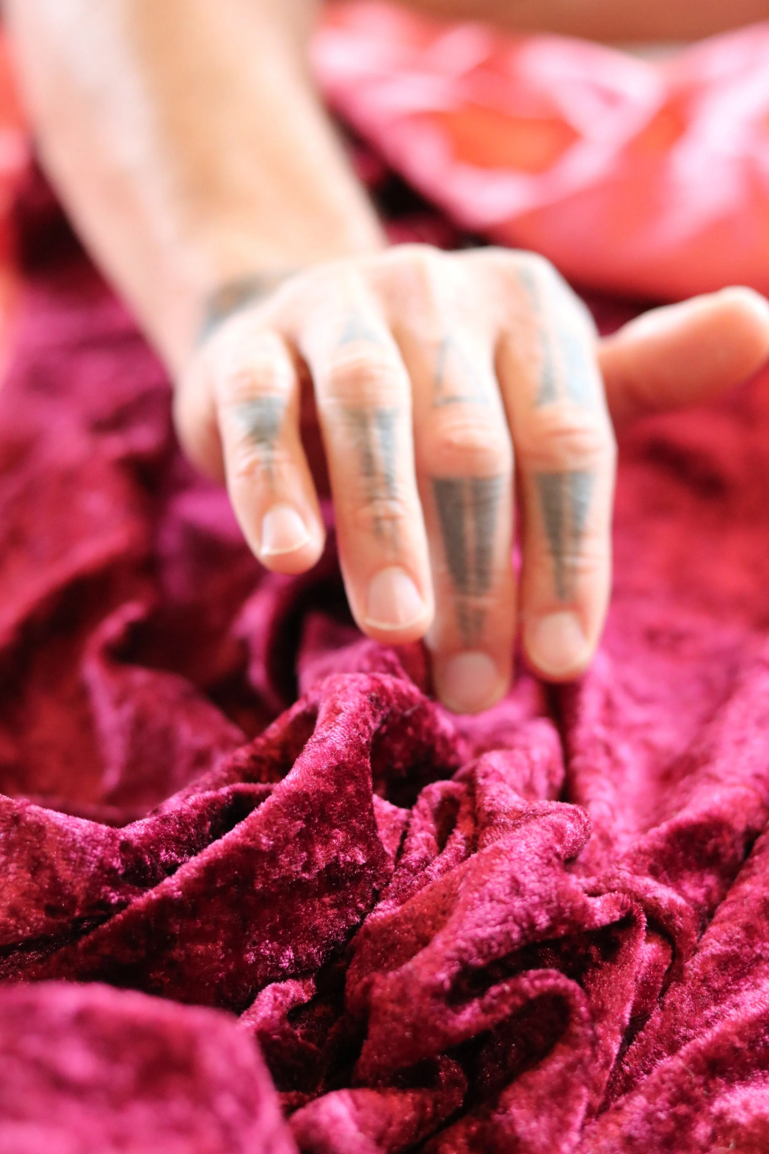 A person's hand with tattoos resting on pink velvet fabric.