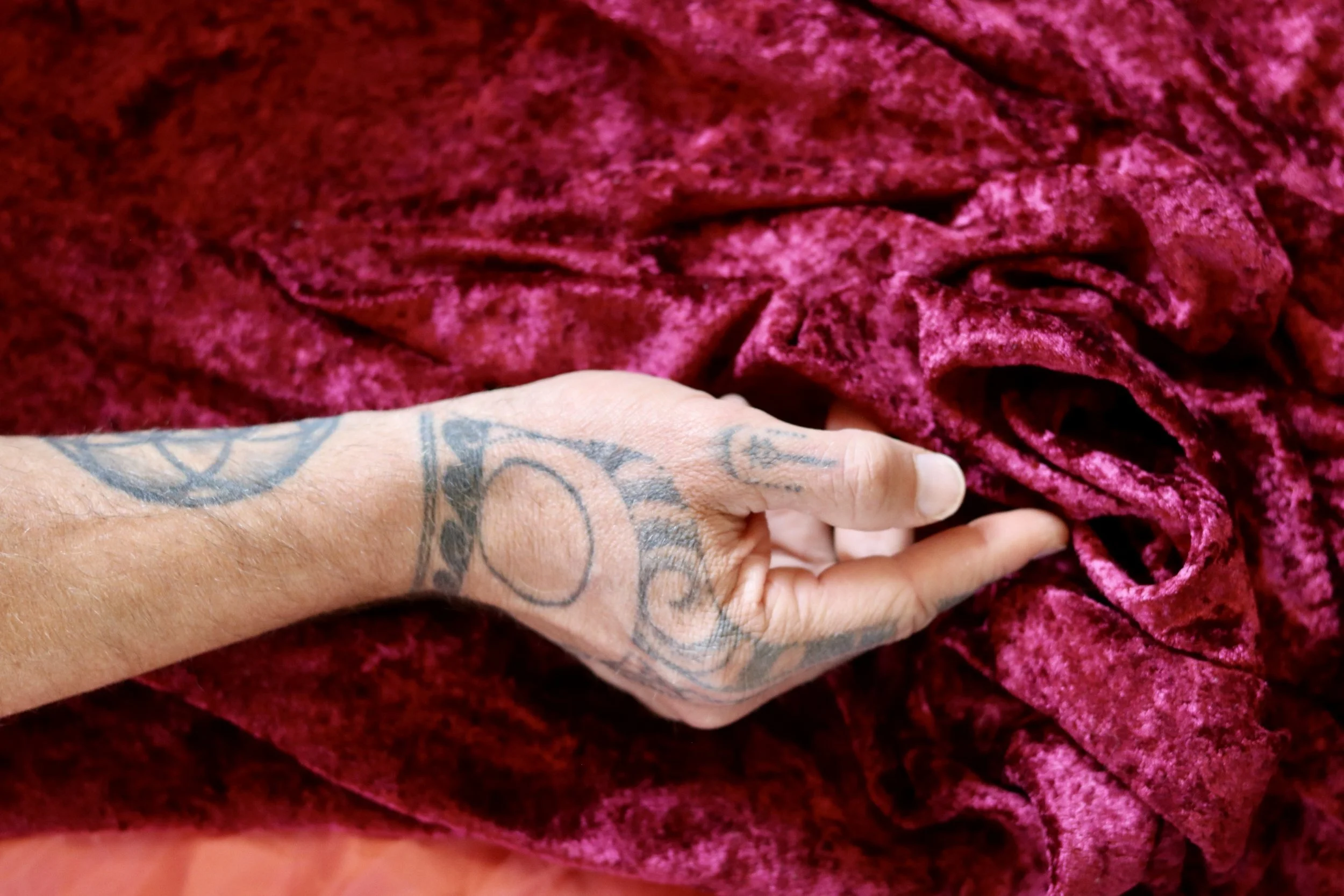 A hand with tattoos grasping a piece of pink velvet fabric.