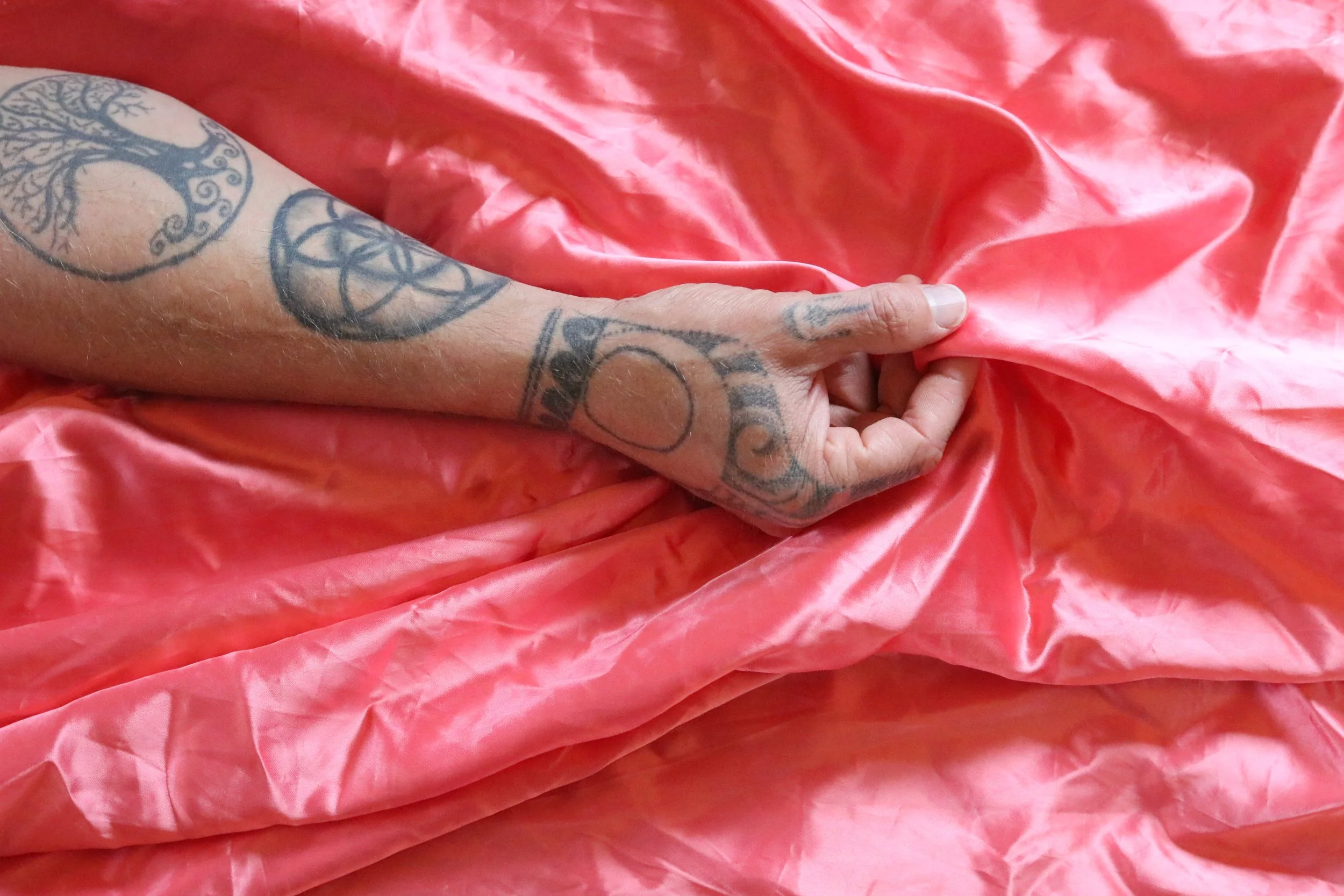 A tattooed arm holding a pink satin fabric.