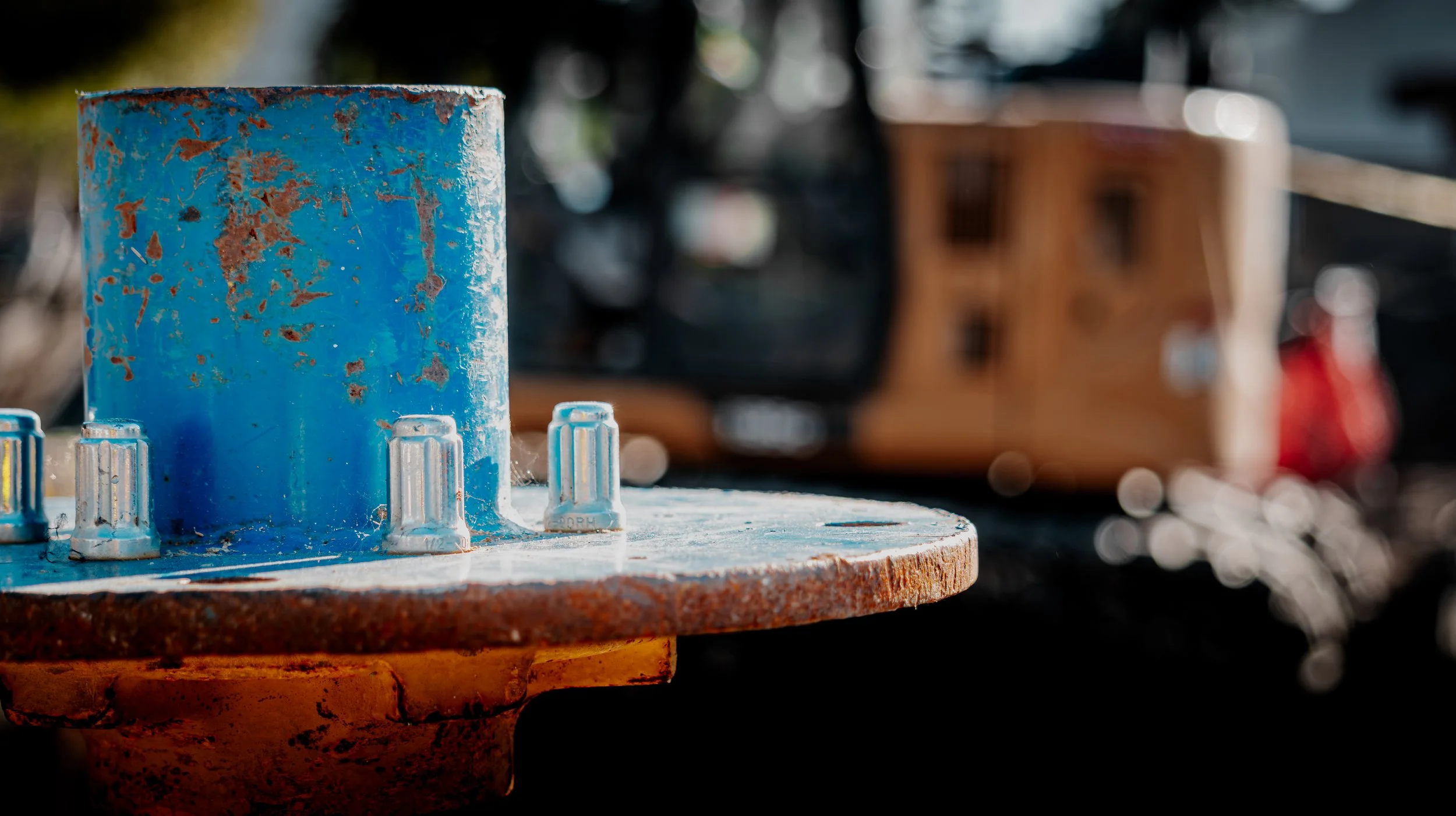 Close-up of a rusty, blue metal spool with white plastic knobs, outdoors with blurred background.
