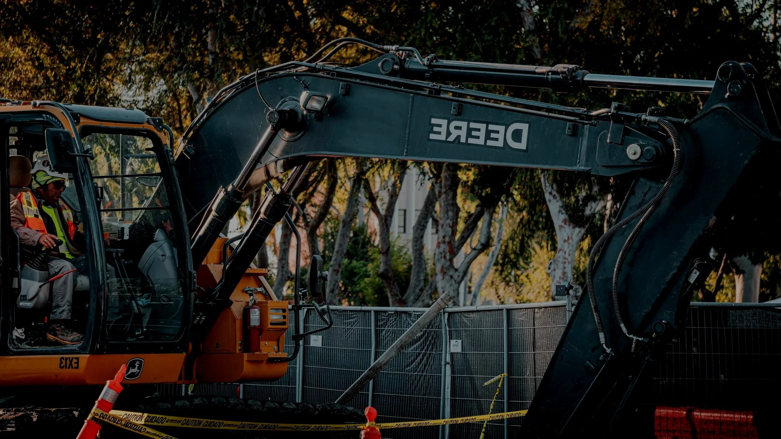 Construction worker operating a large excavator at a work site with safety barriers and caution tape