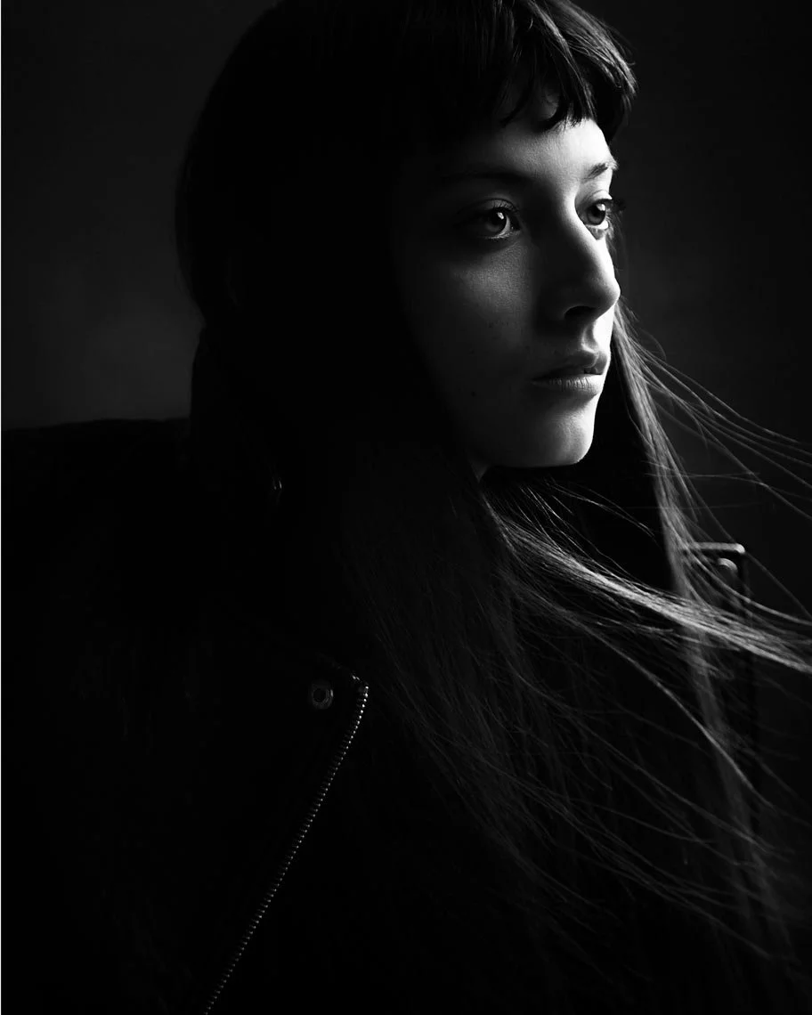 Black and white portrait of a woman with long hair, looking to the right, with soft lighting highlighting her face.