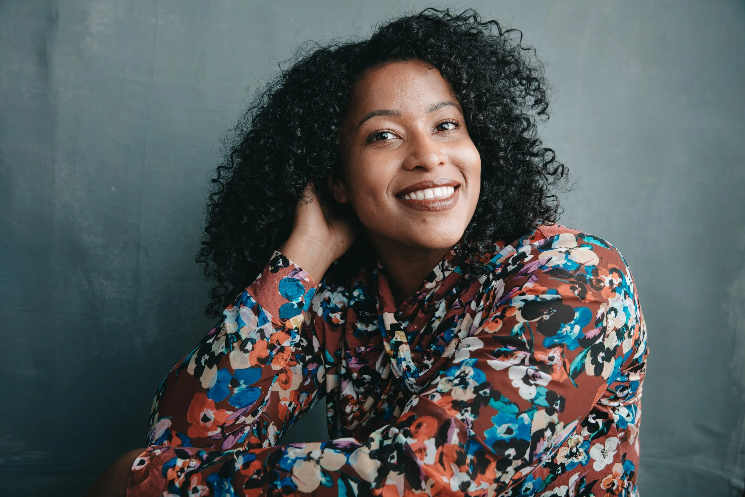 Bright studio portrait of a smiling woman in a colorful floral top against a slate blue wall, San Francisco – Marc Olivier Le Blanc Photography