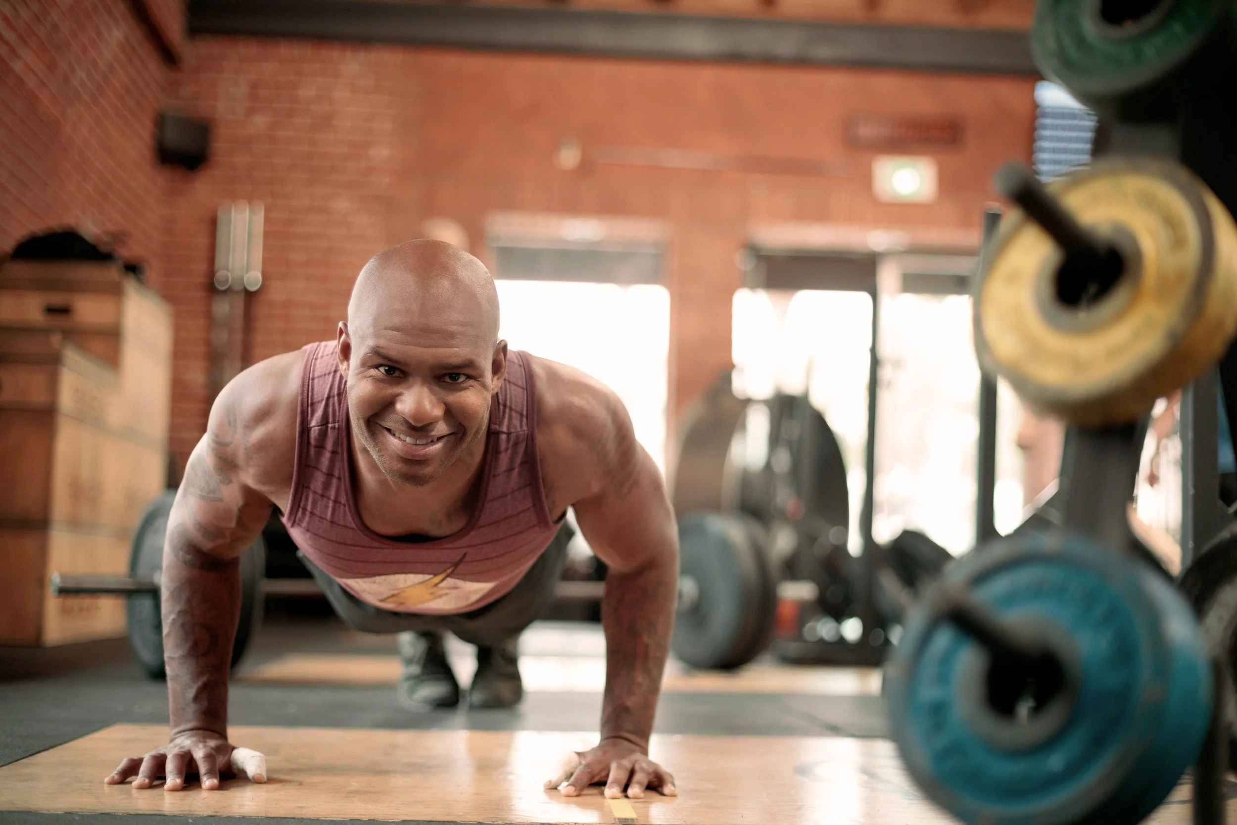 Lifestyle fitness photo of a man doing push-ups and smiling in a brick-walled gym, San Francisco – Marc Olivier Le Blanc Photography
