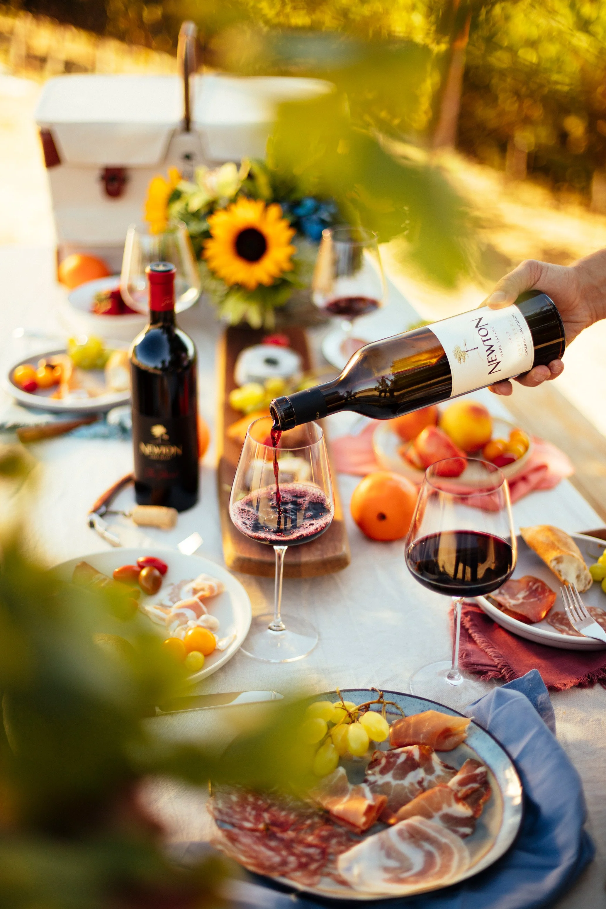Advertising lifestyle photo of Newton red wine being poured at a sunlit outdoor table with charcuterie, Napa Valley – Marc Olivier Le Blanc Photography