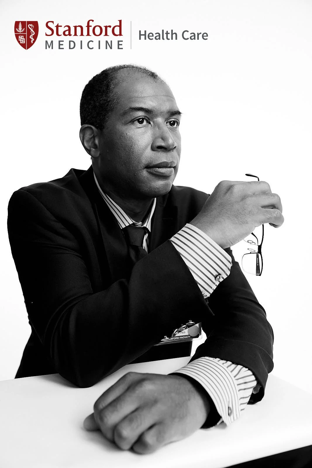 Black and white advertising portrait of a Stanford Medicine Health Care faculty member in a suit holding glasses, San Francisco – Marc Olivier Le Blanc Photography