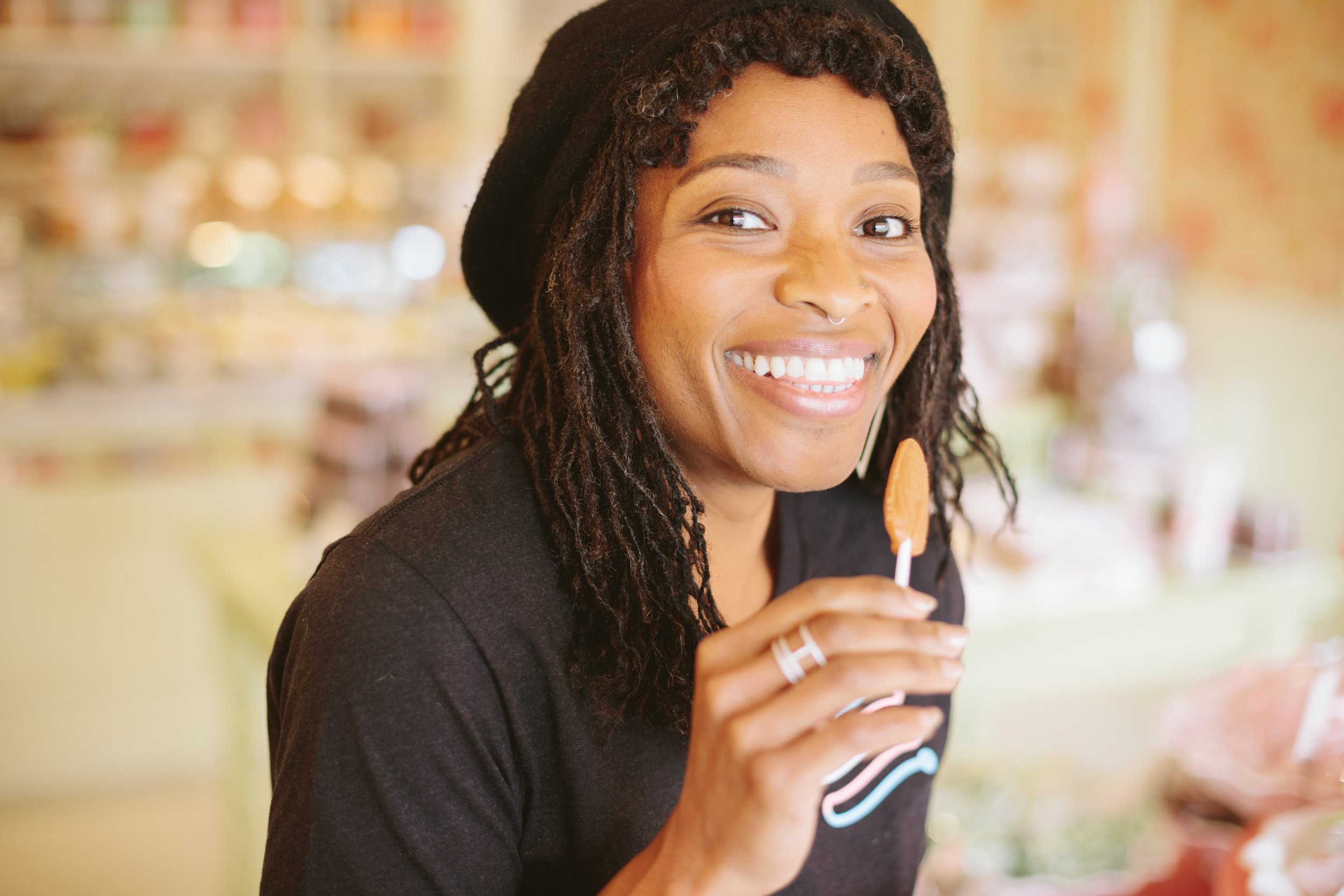 Lifestyle portrait of a smiling young woman holding a lollipop in a colorful San Francisco candy shop – Marc Olivier Le Blanc Photography