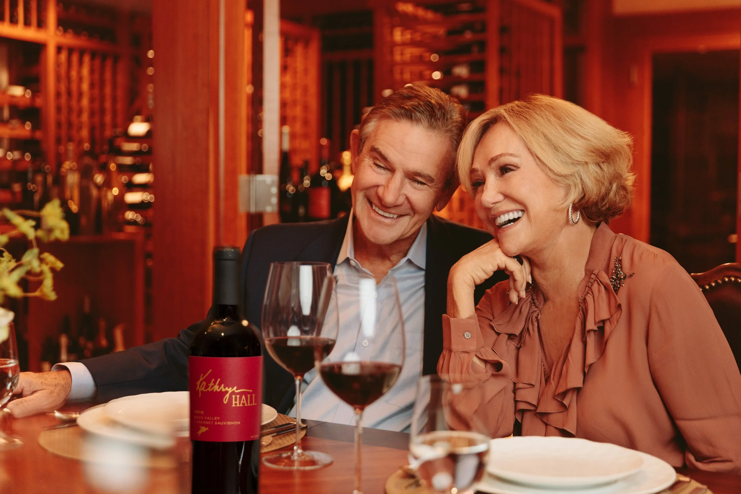 Advertising lifestyle photo of an elegant couple laughing at a candlelit wine dinner in a Napa Valley wine cellar for Kathryn Hall winery – Marc Olivier Le Blanc Photography