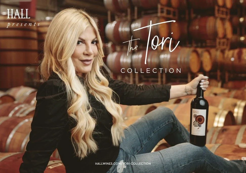 Advertising campaign photo for Hall Wines Tori Spelling Collection featuring a woman seated with a wine bottle in a Napa Valley barrel room – Marc Olivier Le Blanc Photography
