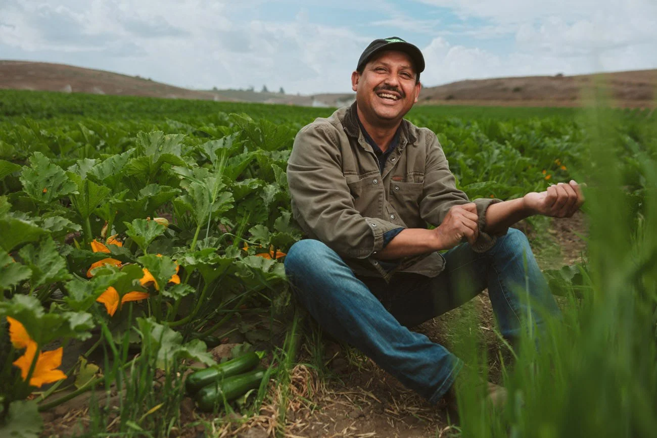 Advertising portrait of a smiling farmer sitting in a lush vegetable field in California – Marc Olivier Le Blanc Photography