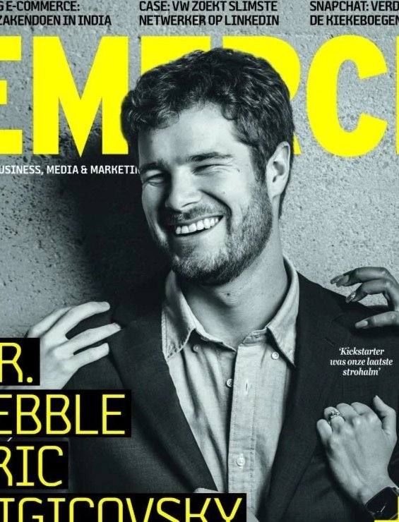 Black and white magazine cover featuring a smiling man with curly hair, wearing a blazer and shirt, against a textured background, with bright yellow and white text.