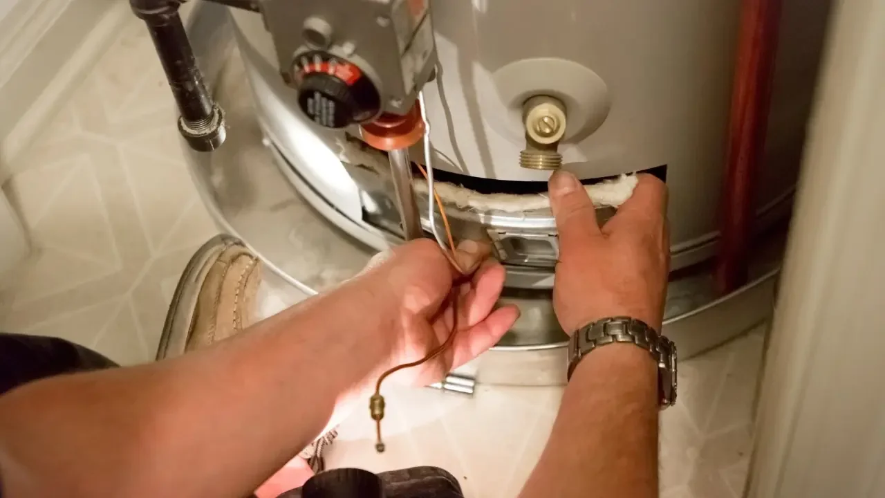 A technician opening a water heater. One hand is opening a hatch while another holds wires.