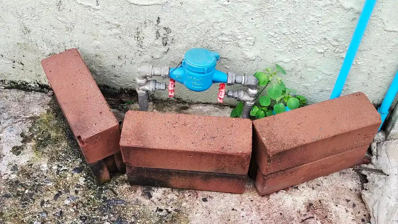 A backflow preventer that was recently installed just outside of a home. It is surrounded by a small wall of bricks to protect it.