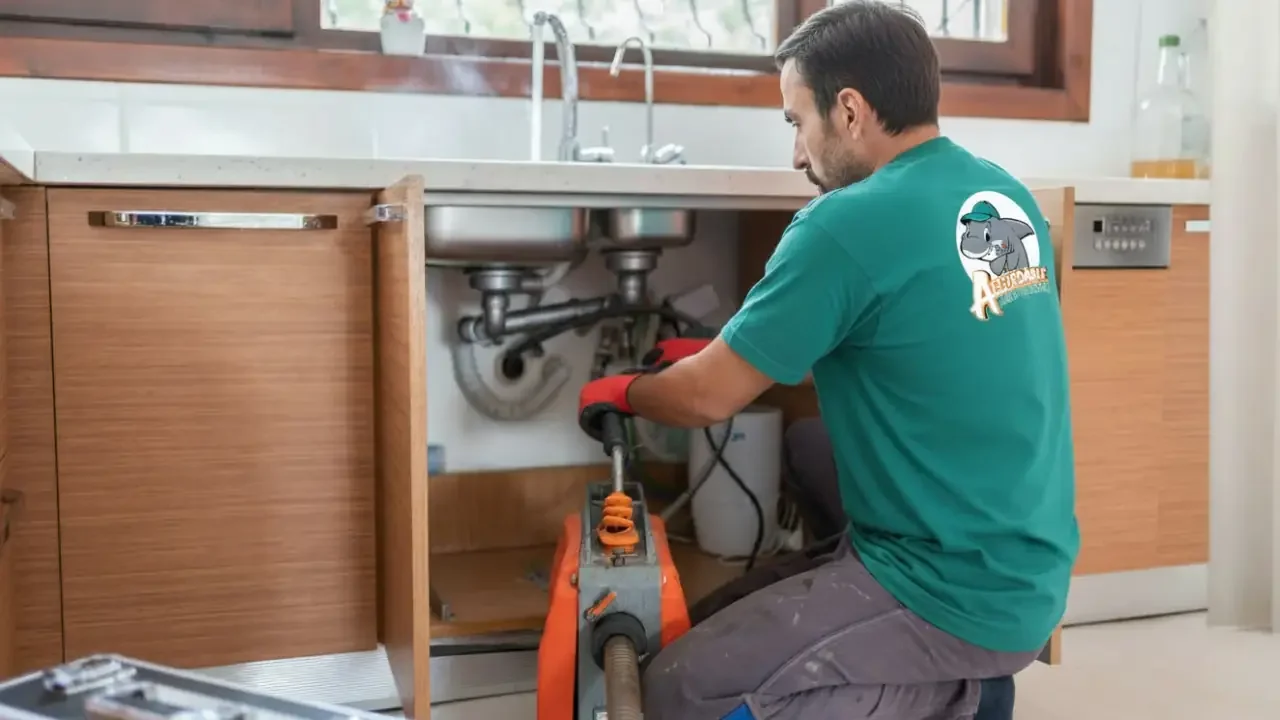 An Affordable Air and Plumbing Drain cleaning technician cleaning a kitchen sink drain with a mechanical drain auger.