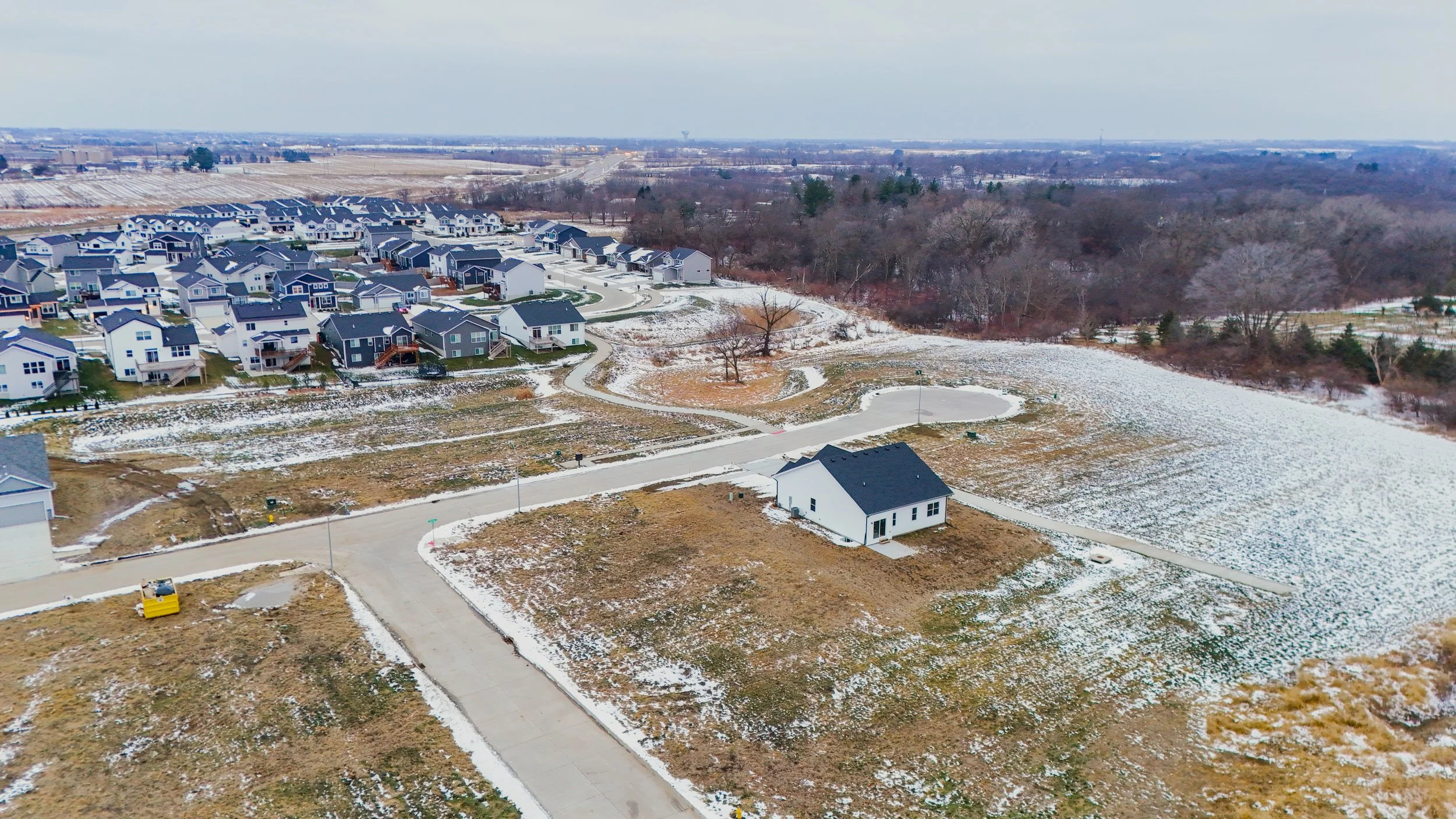 Aerial view of a new residential neighborhood with houses, roads, and patches of snow on the ground during winter.