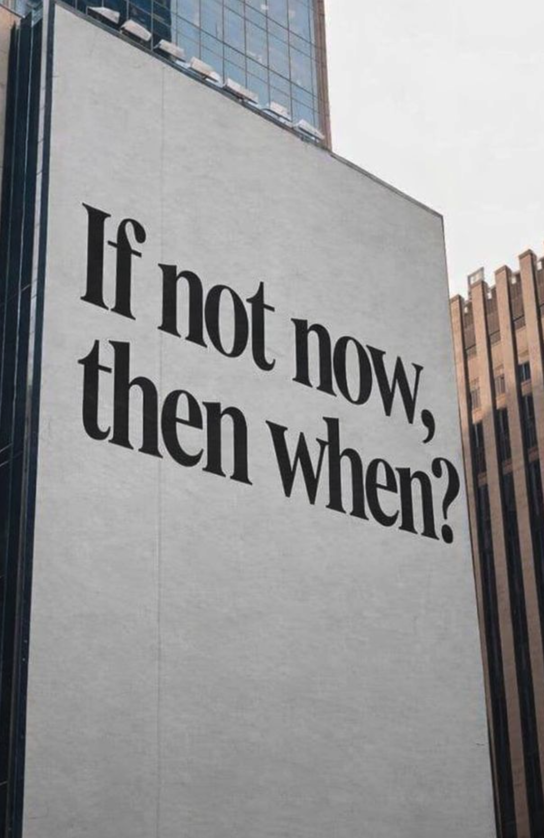 Large billboard on a tall building displays the quote, 'If not now, then when?' in black bold text against a white background, with other buildings nearby.