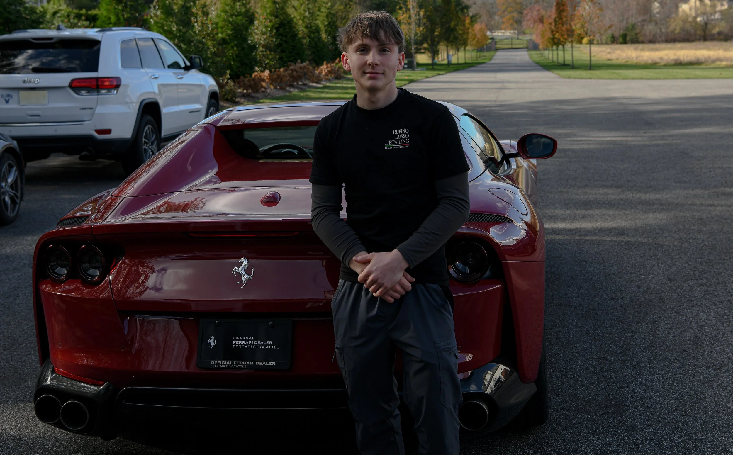 A young man standing in front of a red Ferrari sports car parked after being detailed.