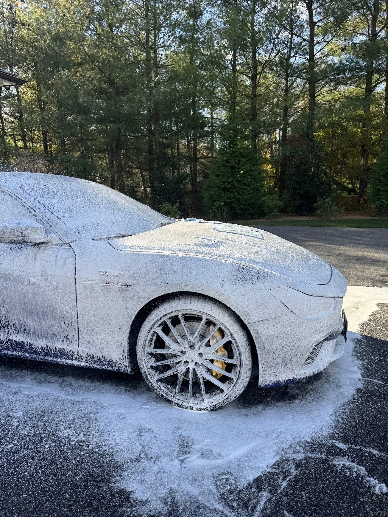 White Maserati sports car covered in soap suds during a car detail outside on their driveway.