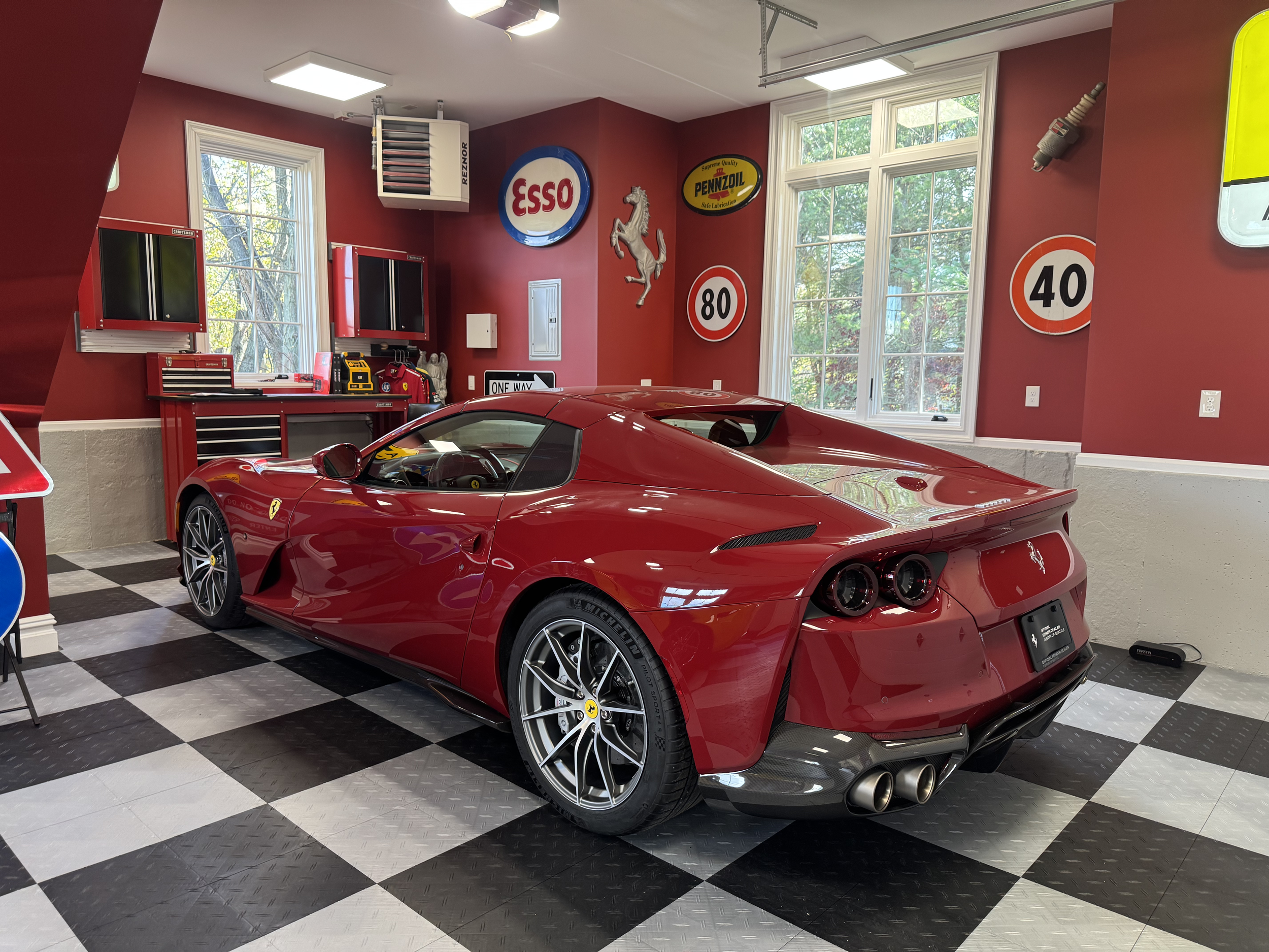 Red Ferrari 812 superfast gts from a valued client, parked inside a clients garage with checkered black and white floor, red walls, and vintage signs, including Esso, Pennzoil, and speed limit signs.