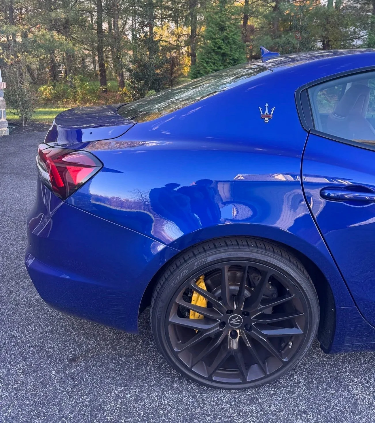 Rear half of a blue Maserati sports car parked , yellow brake caliper visible through black alloy wheel, and Maserati emblem on the side.