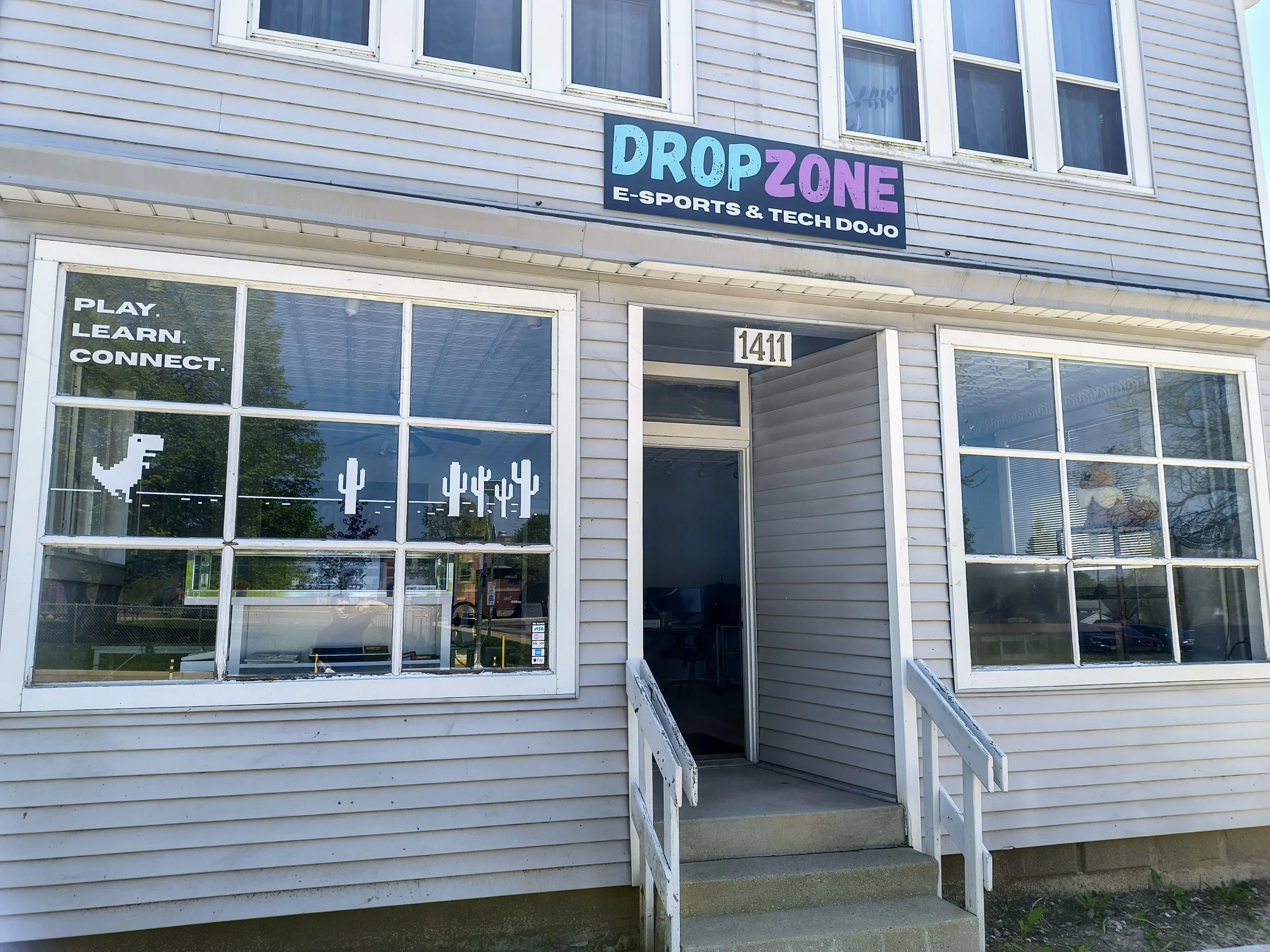Front exterior of a building with a sign reading 'DropZone E-Sports & Tech Dojo,' with a glass door and windows, and the address number 1411 above the door.