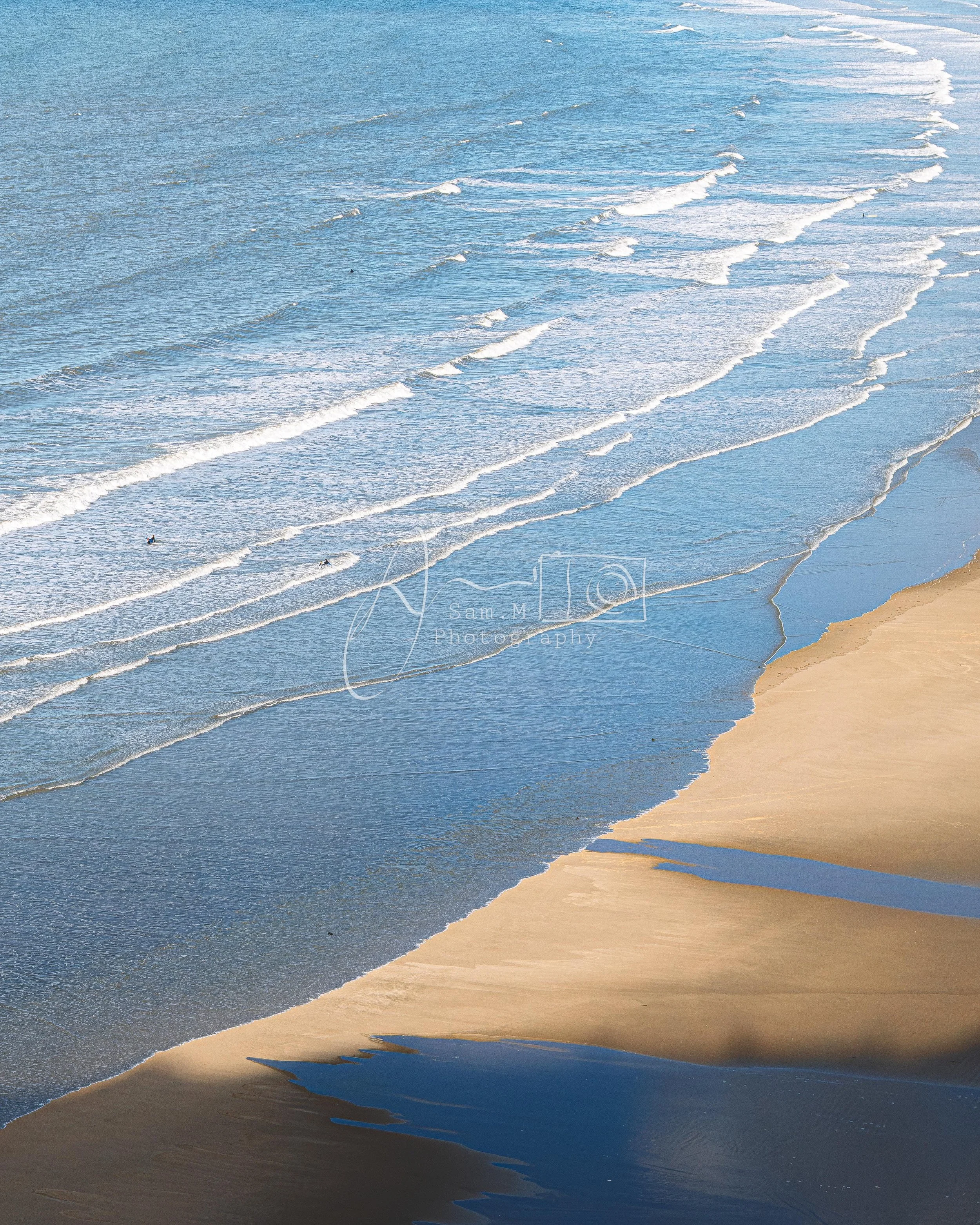 Aerial view of a beach with waves crashing onto the sandy shore, showing sea and sand meeting.