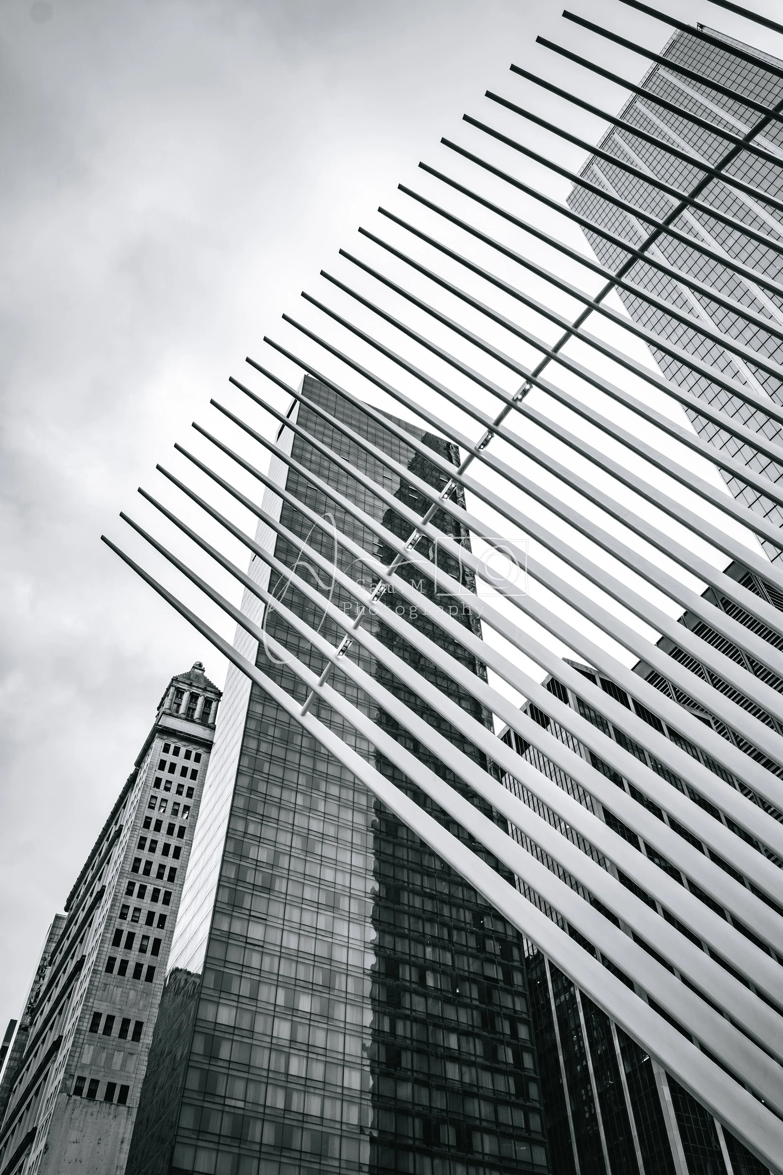 Black and white photo of modern skyscrapers, one with a notable vertical spire, and another with a metal grate or louver structure in the foreground.