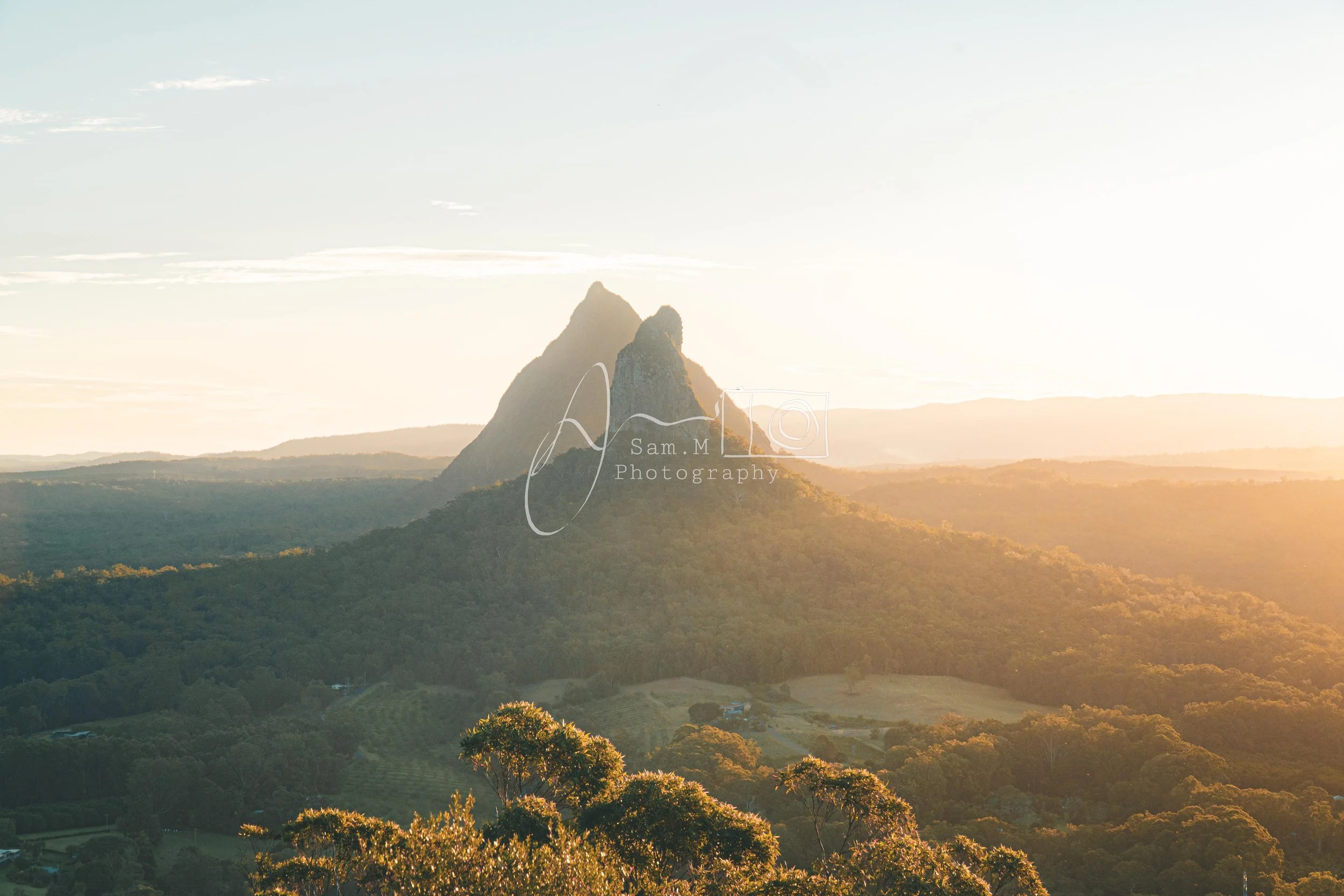 Scenic view of a mountain landscape during sunset with a prominent pointed mountain peak and a forested valley in the foreground.