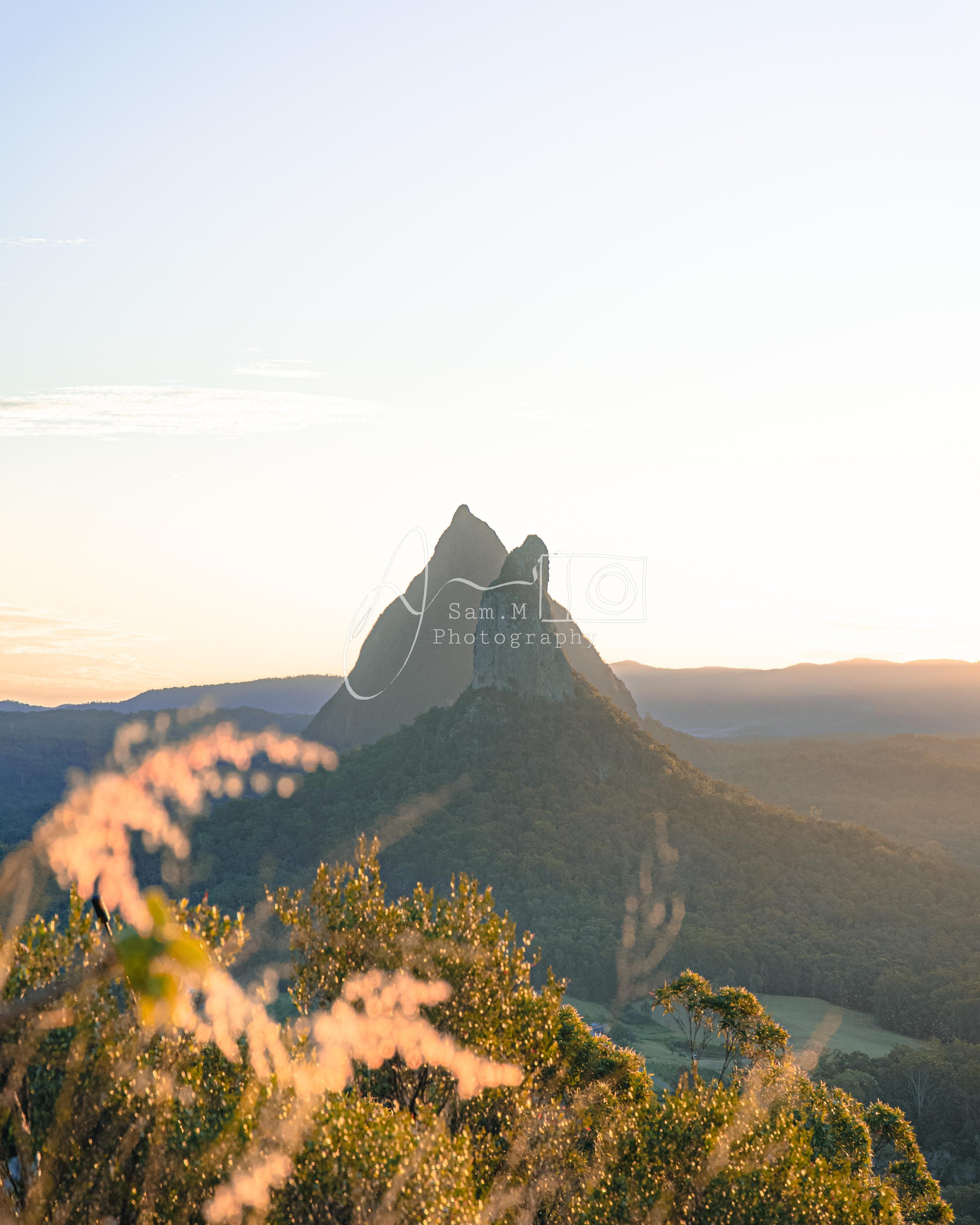 Sunset over a mountain range with prominent peaks and lush greenery in foreground.