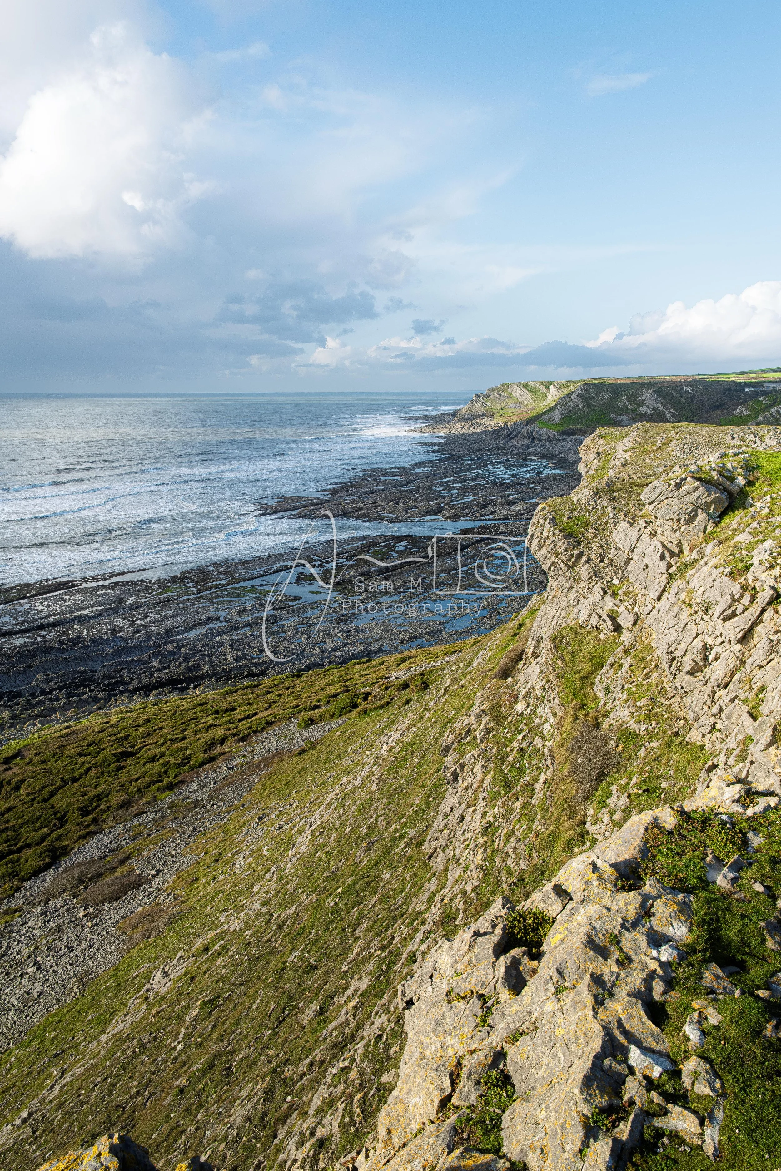 Cliffs overlooking a rocky shoreline and the ocean under a partly cloudy sky.
