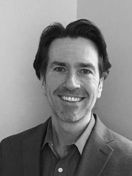 Black-and-white headshot of Eoin O'Carroll in a blazer. The photo doesn't show it, but he's also wearing nice pants.