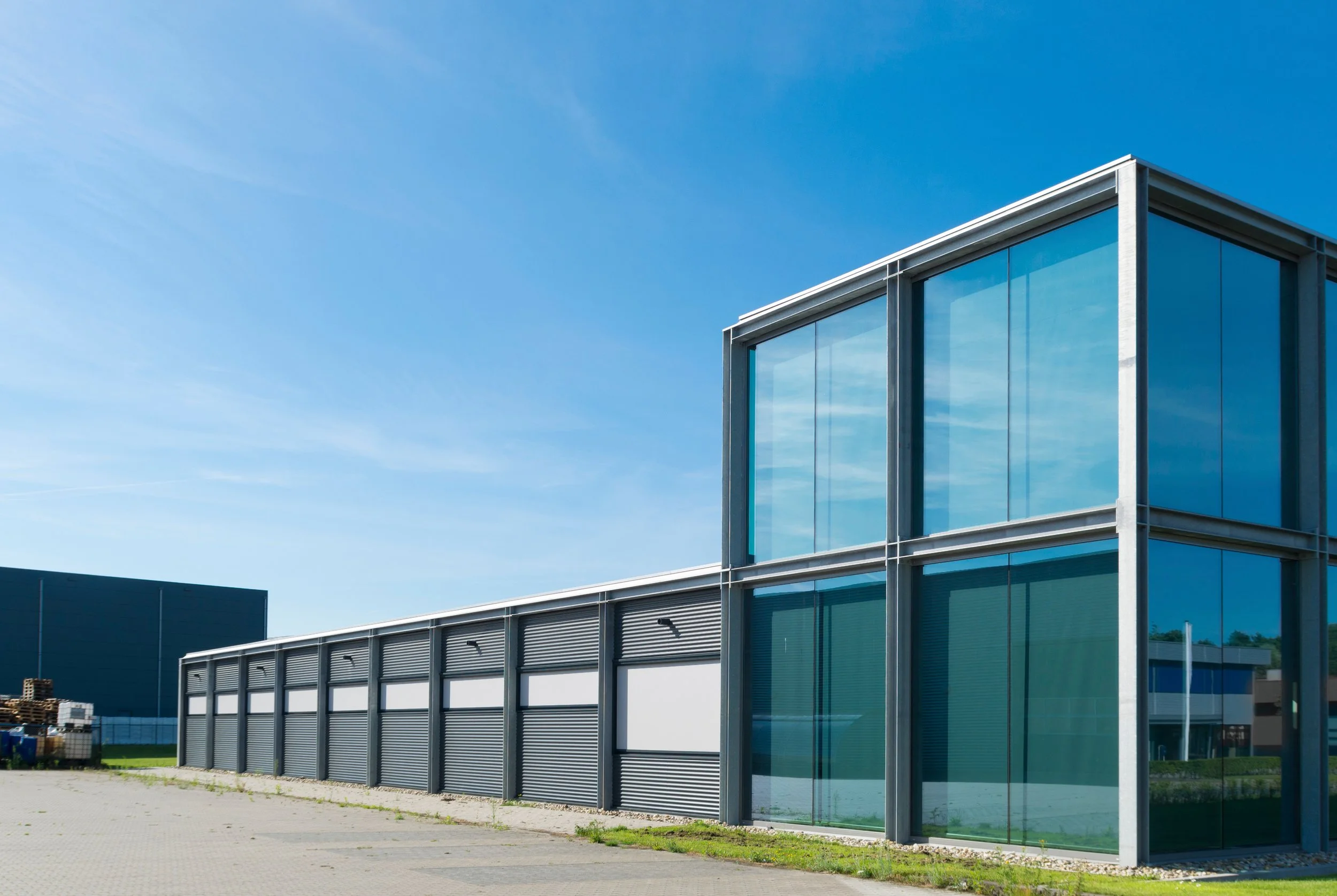 Modern building with glass walls and roller shutter doors under a clear blue sky.
