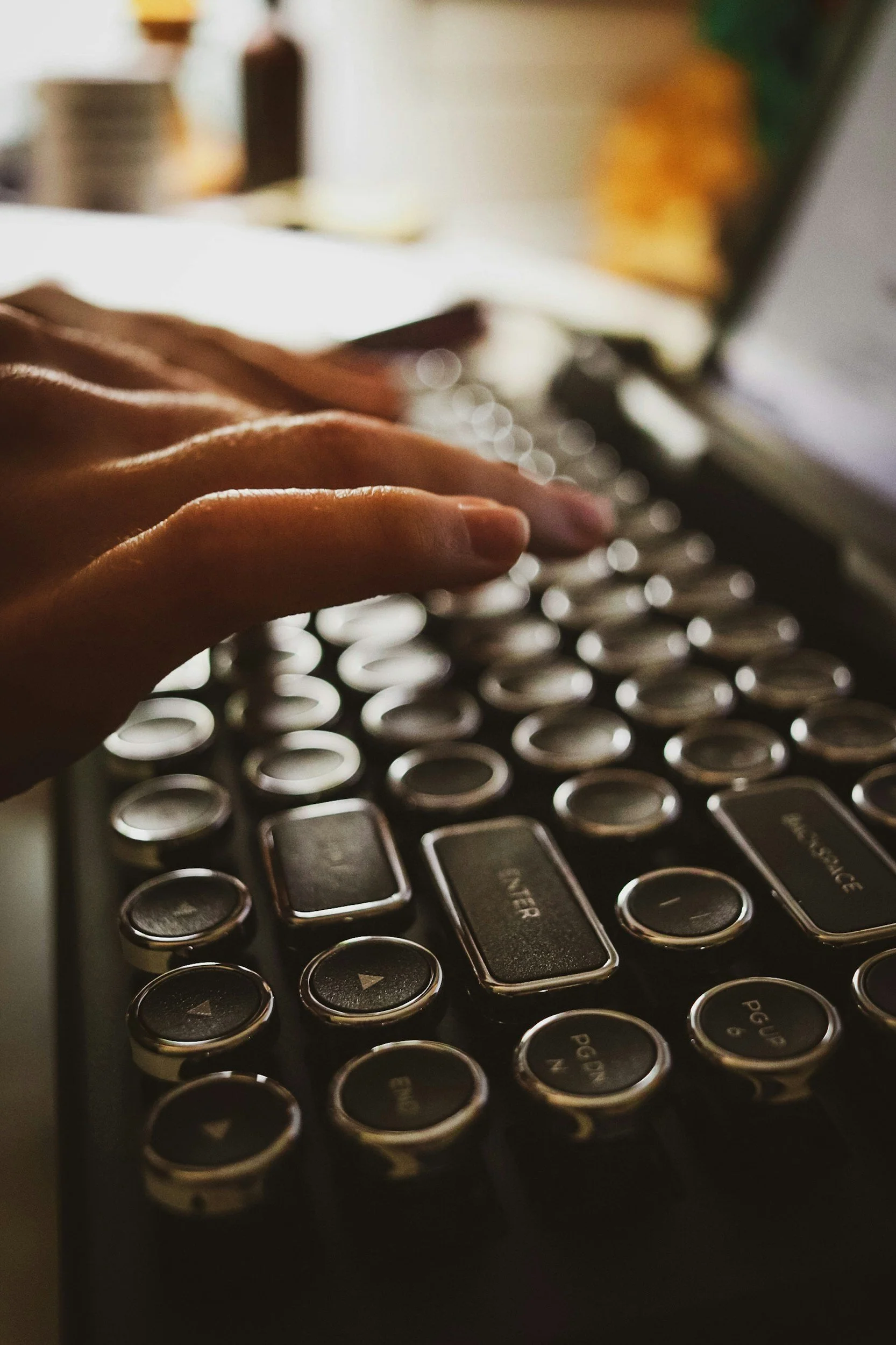 Close-up of a person's hand typing on a black computer keyboard with circular keys, with a blurred background.