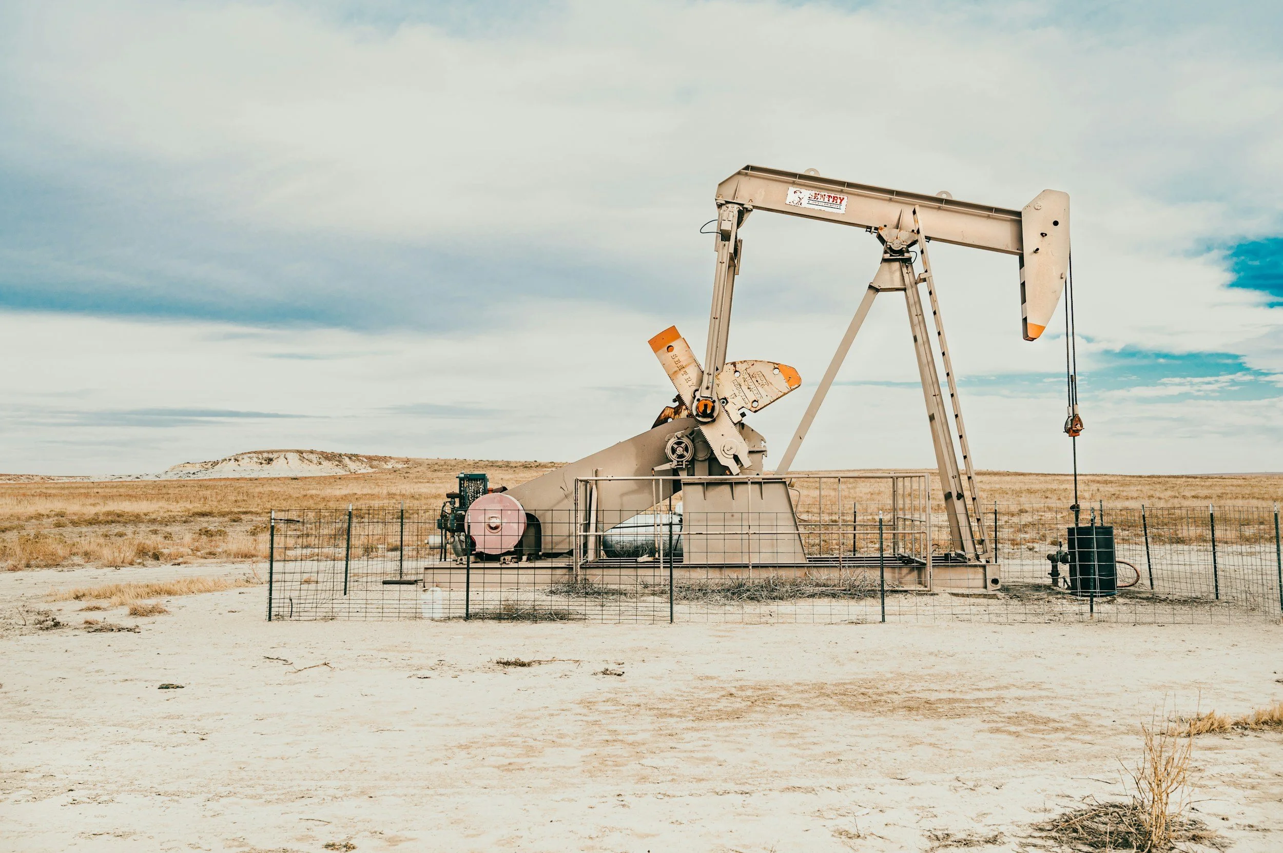 An oil pumpjack in a barren desert landscape under a cloudy sky.